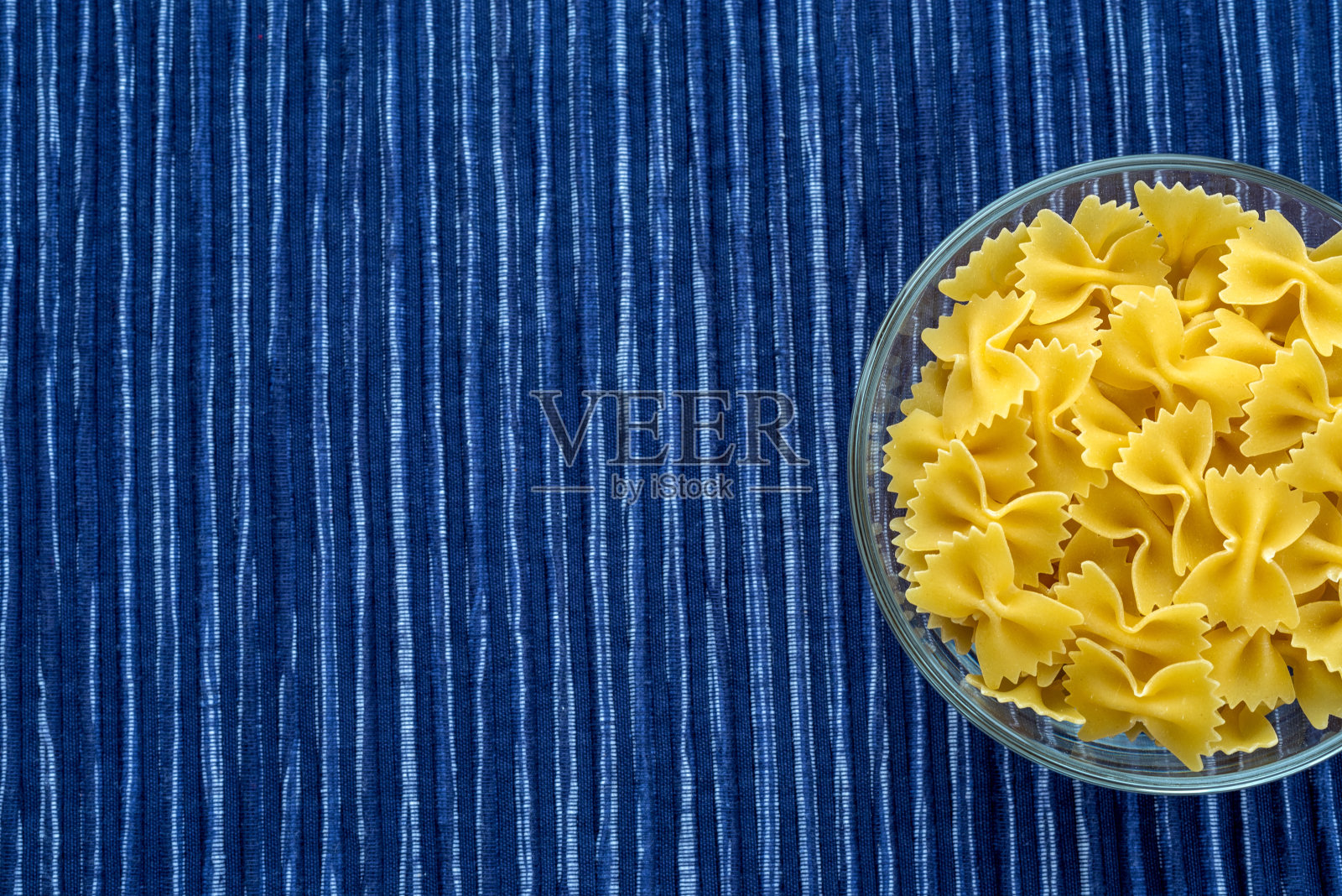 法法尔通心粉通心粉在一个玻璃杯上条纹白色蓝色的布背景与一边。上面的特写。为文本留出空间。照片摄影图片