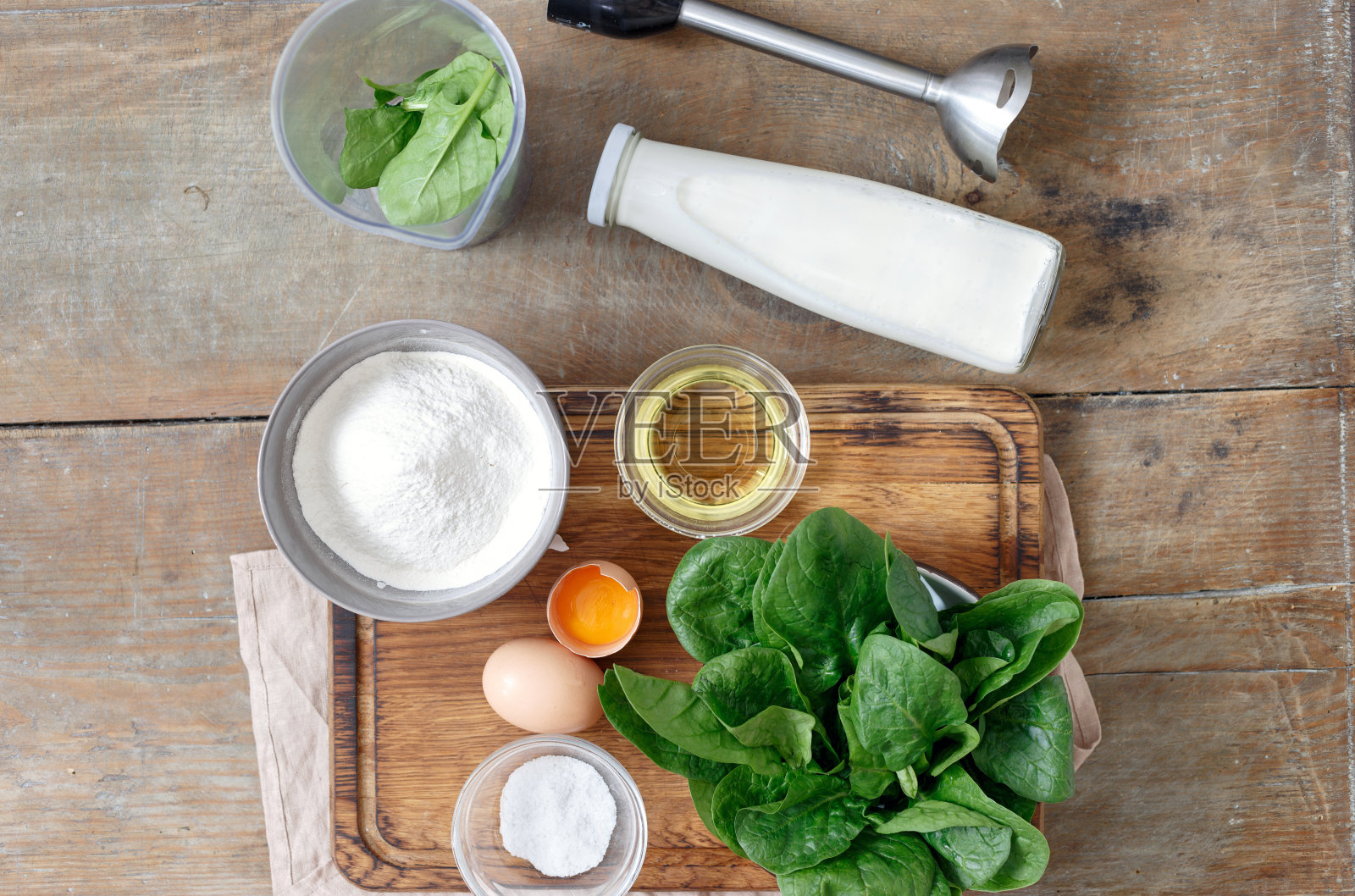 一套烹饪菠菜煎饼的配料(面粉、鸡蛋、油、牛奶和菠菜叶)放在木桌上，俯视图照片摄影图片