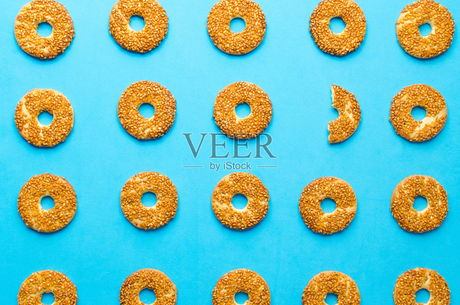 蓝色背景上有芝麻的圆形曲奇，一个曲奇并不像所有的曲奇那样。照片摄影图片