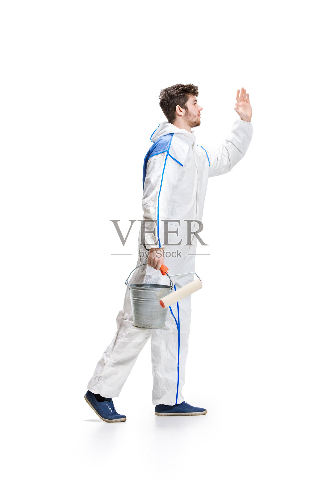 年轻的男性装饰师用油漆滚轮爬上了一个梯子孤立的白色背景照片摄影图片