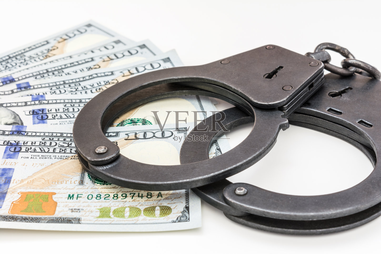 黑色金属手铐躺在白色背景的100美元钞票上照片摄影图片