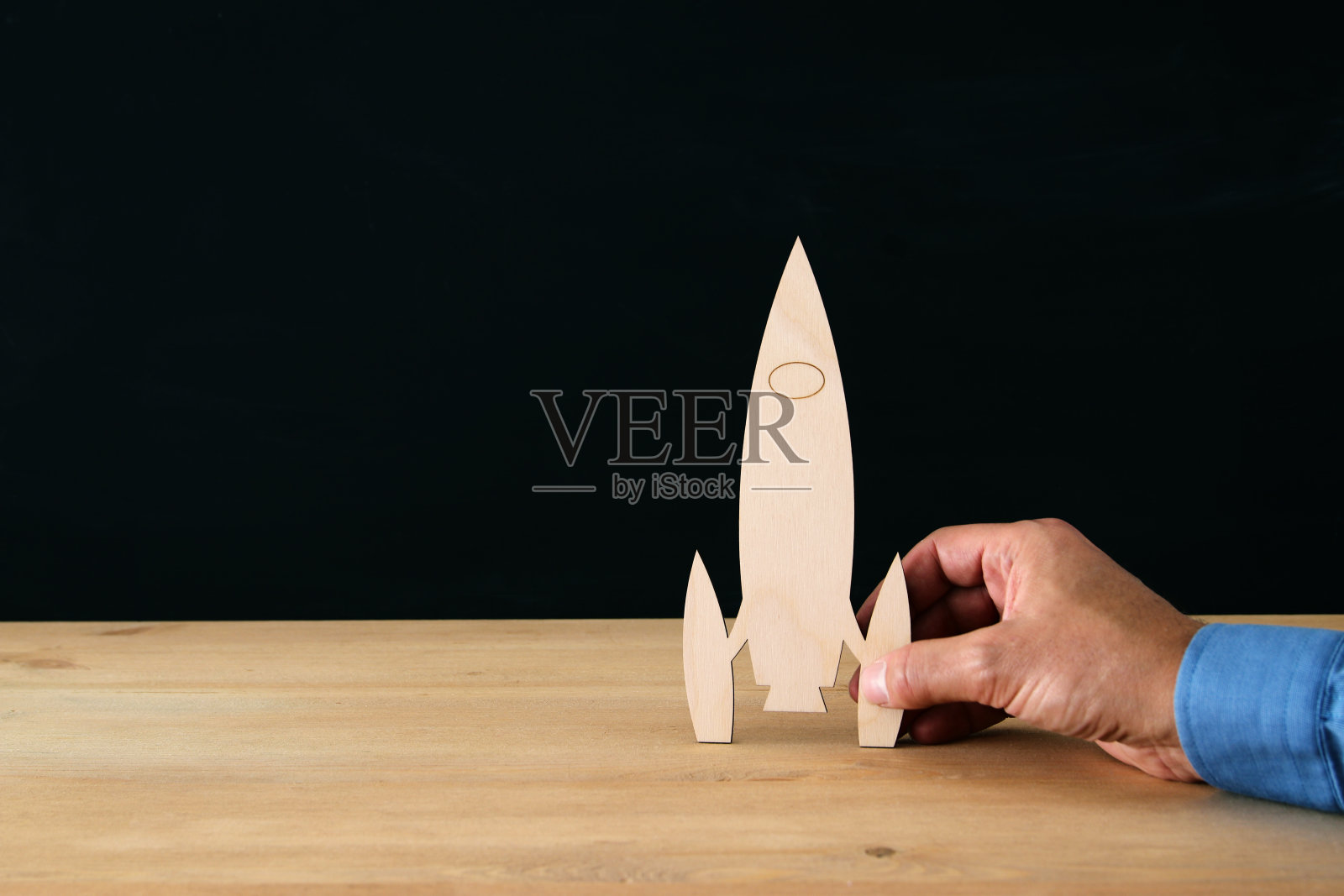 男子手握木制火箭，越过黑色背景。照片摄影图片