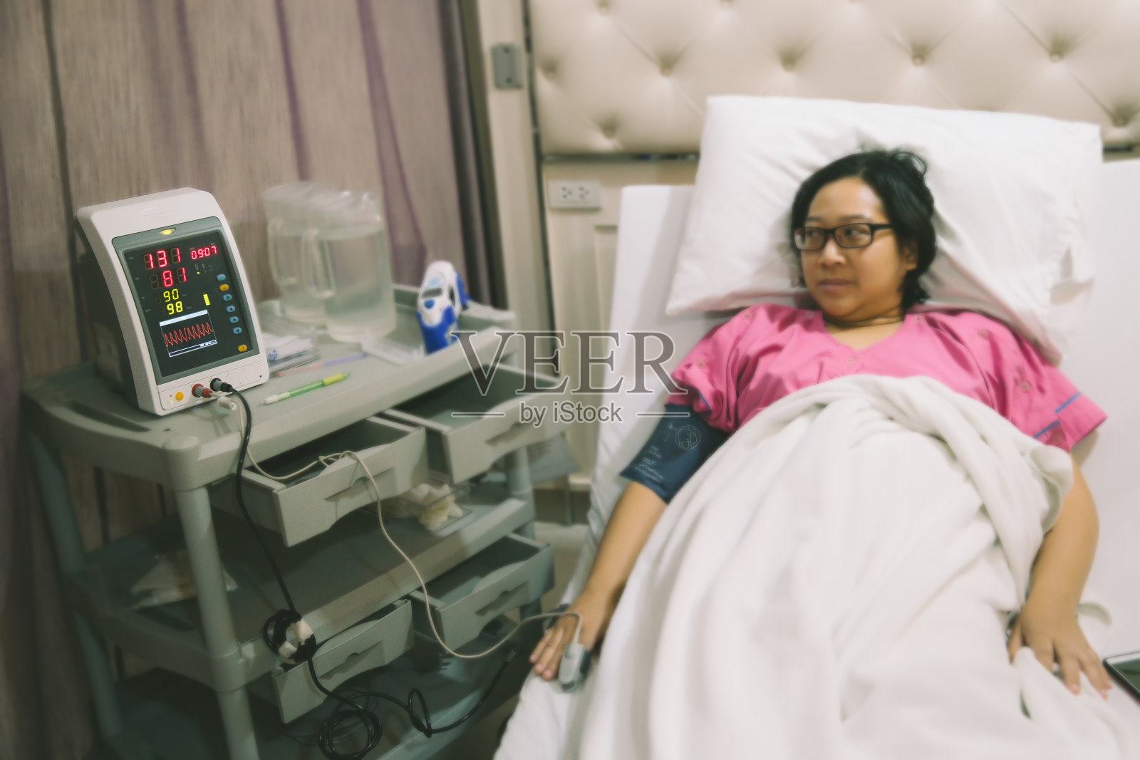 妇女躺在医院的病床上，配有心率医疗设备。照片摄影图片