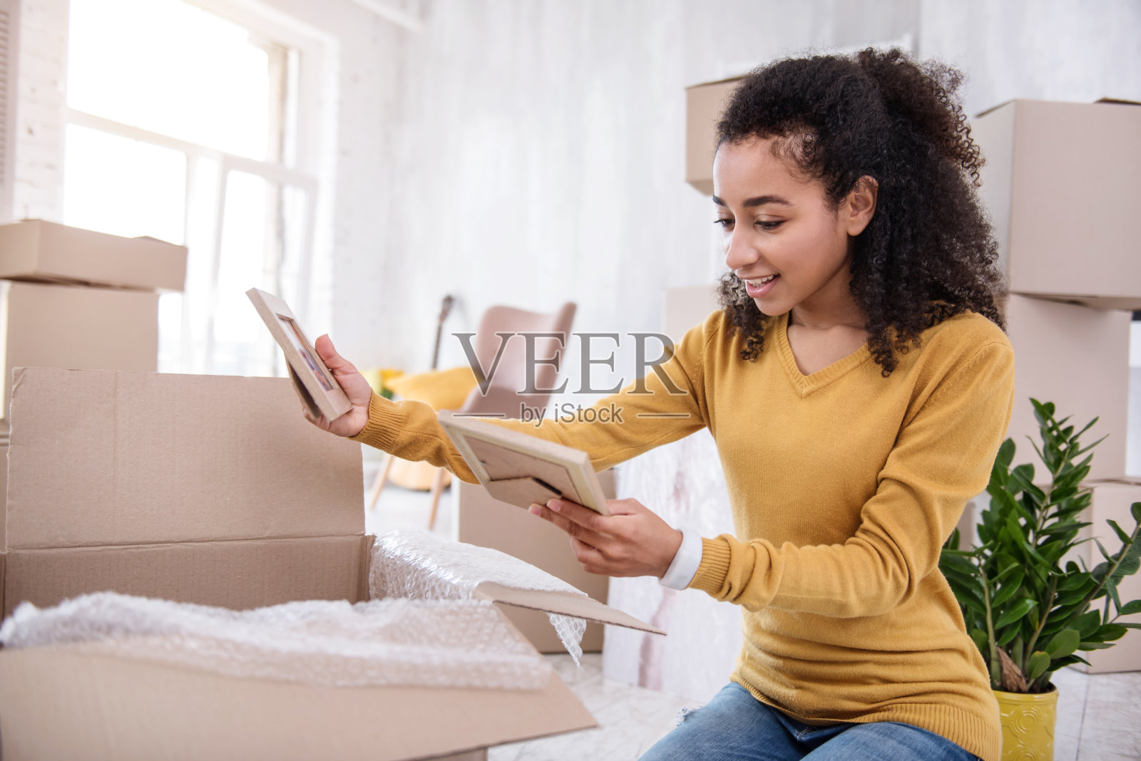 卷头发的女孩一边打包一边翻看相框里的照片照片摄影图片