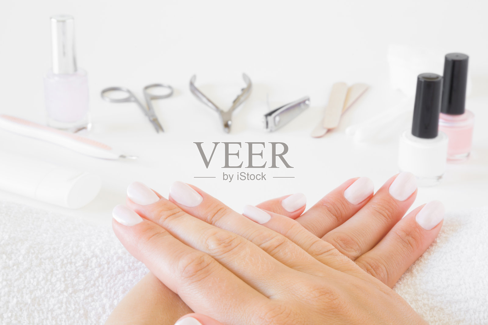 年轻，完美，整洁的女人的手和白色指甲在毛巾上。桌子上有一套钉工具。手护理。修指甲、修脚美容沙龙。照片摄影图片