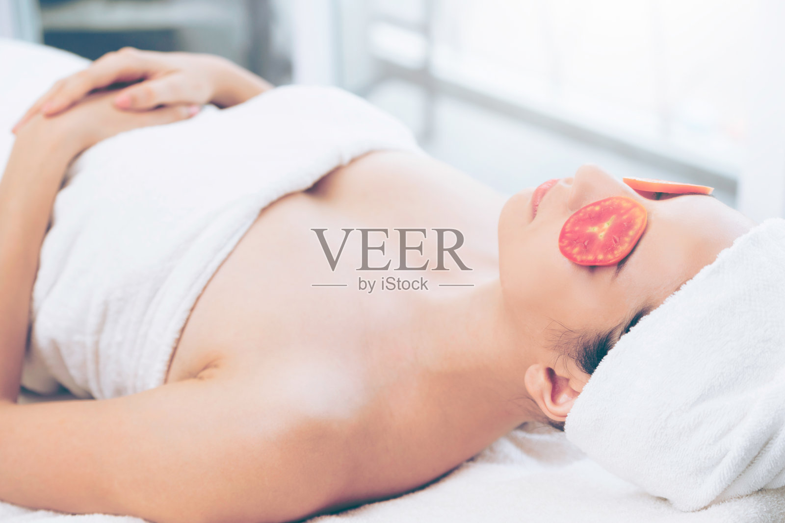 女人正在用番茄进行眼部自然治疗。照片摄影图片