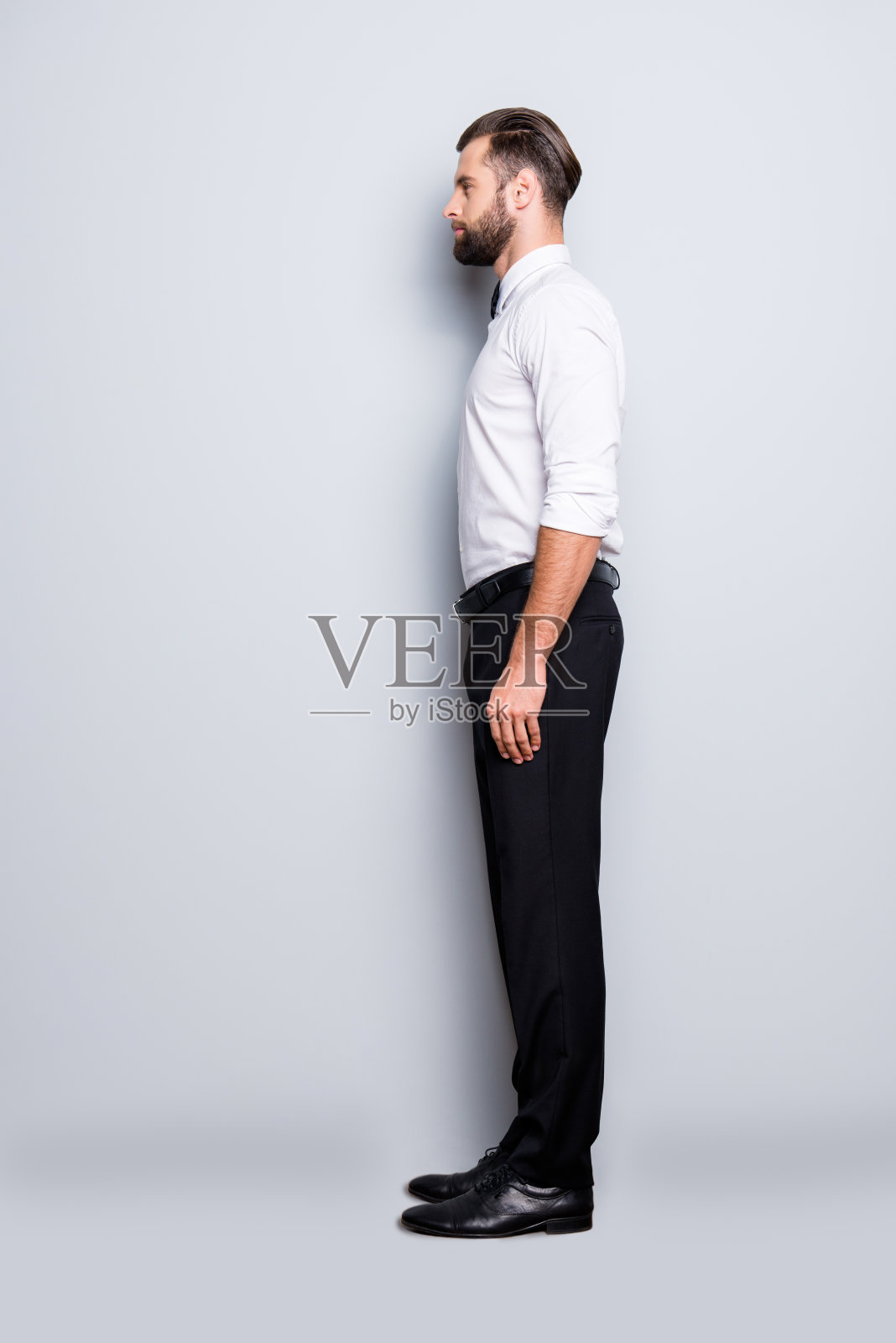 全尺寸的全身半脸肖像帅气时髦的赌场老板在白色衬衫，领结，黑色裤子，正装，孤立在灰色背景照片摄影图片