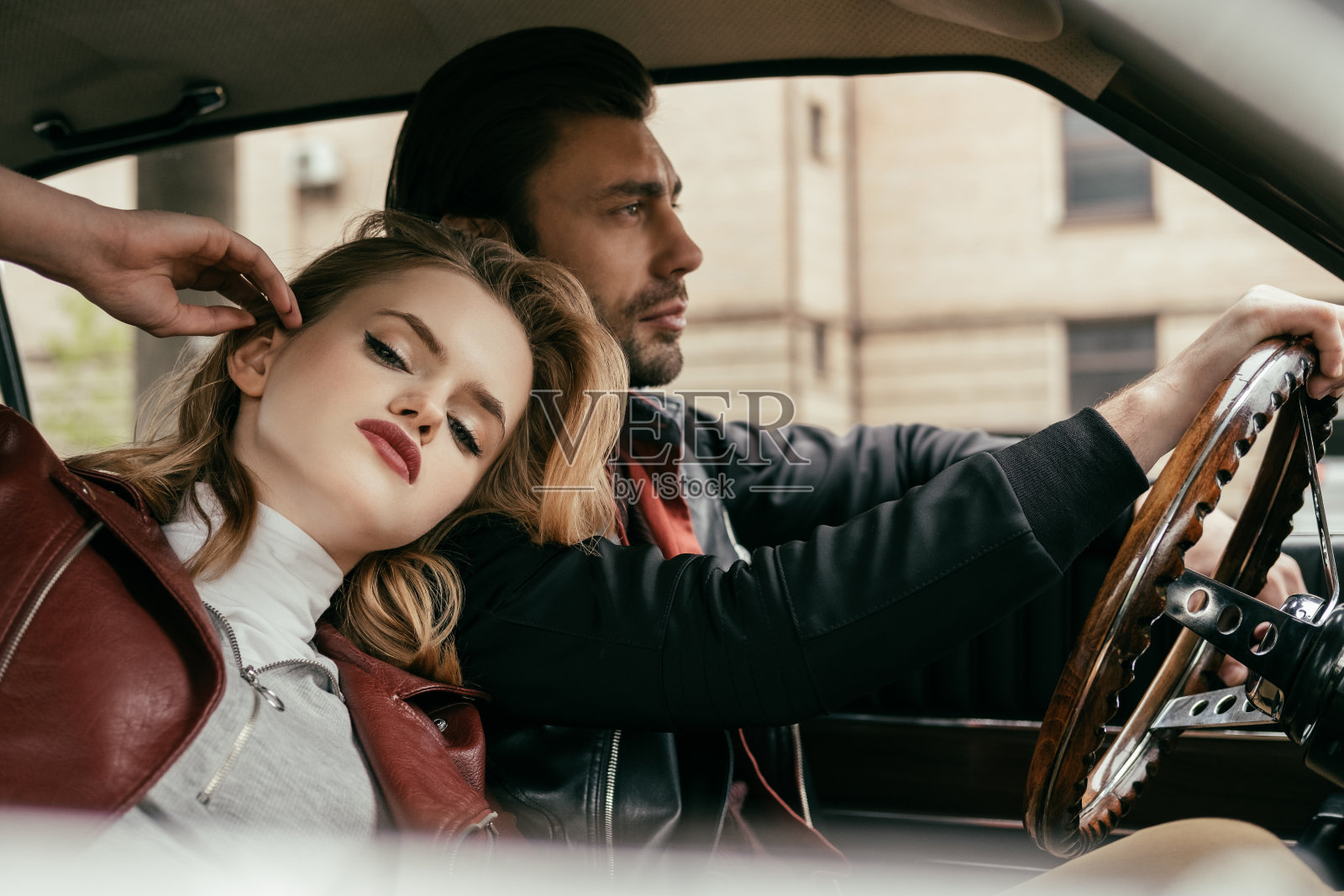 性感的年轻女人看着镜头，而男朋友开着老爷车照片摄影图片