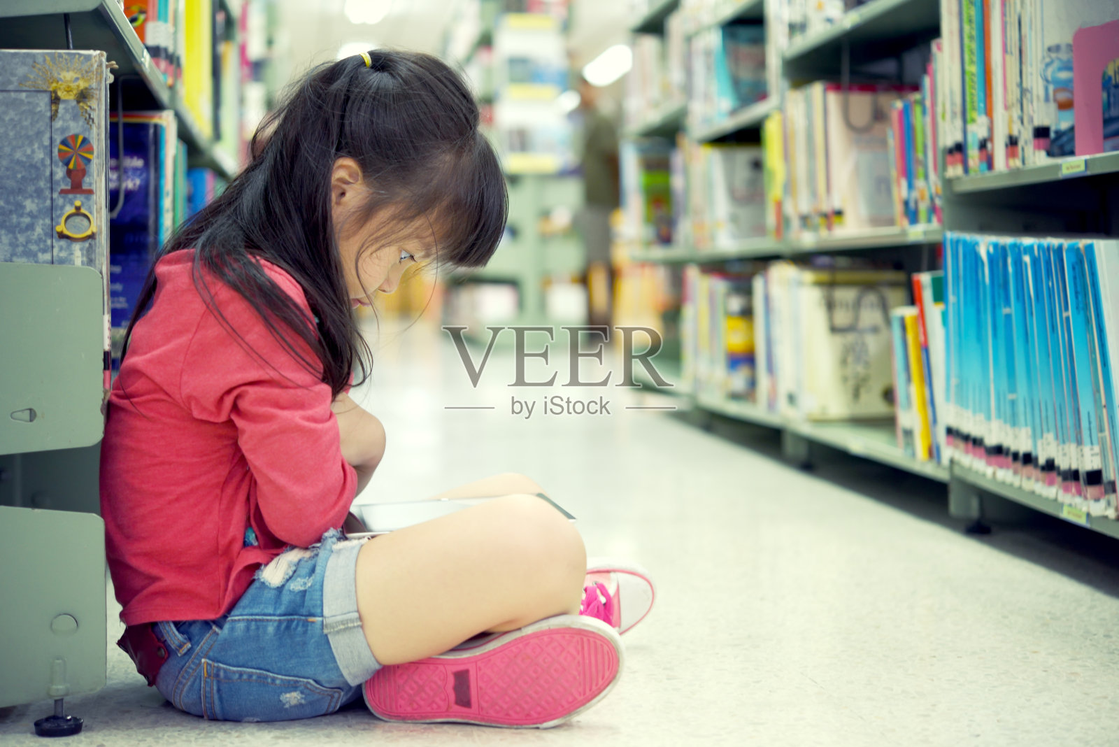 可爱的小女孩在图书馆看书。照片摄影图片