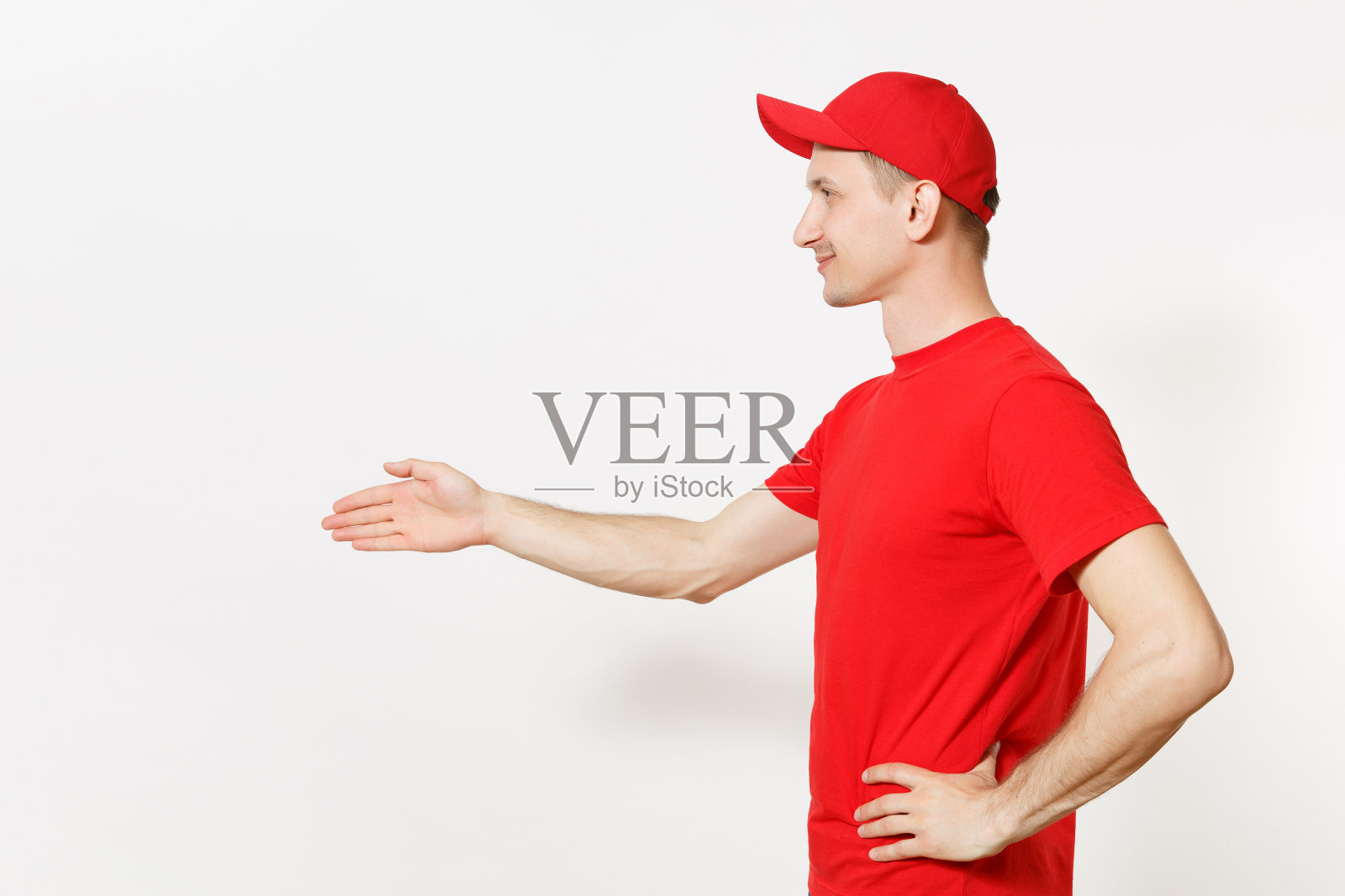 身穿红色制服的送货员被隔离在白色背景下。专业友好的男性戴着帽子、t恤作为快递员或经销商，站着伸出手来问候。复制广告空间。照片摄影图片
