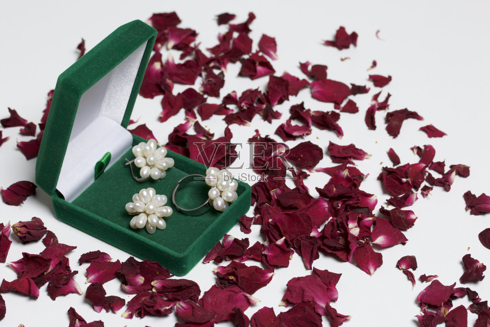 一个开放的绿色天鹅绒珠宝盒。里面有一套:一枚戒指和镶着珍珠的耳环。在白色的背景上，撒着干玫瑰花瓣。照片摄影图片