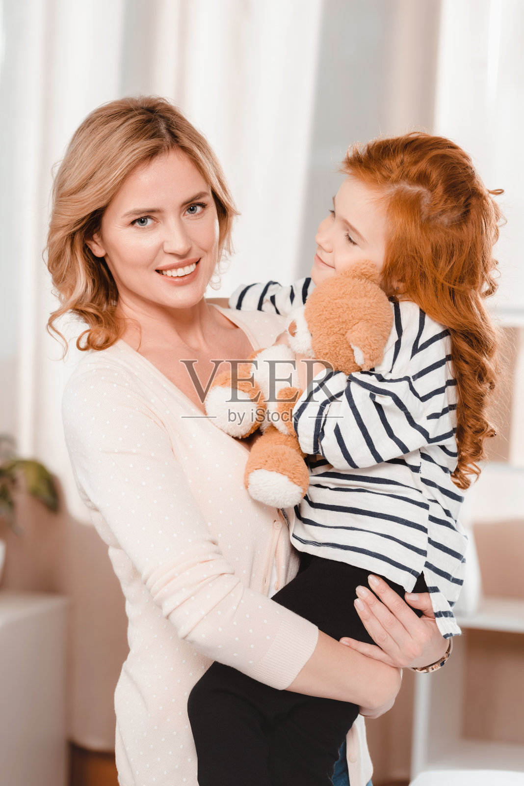 微笑的母亲抱着小女儿和泰迪熊的肖像照片摄影图片