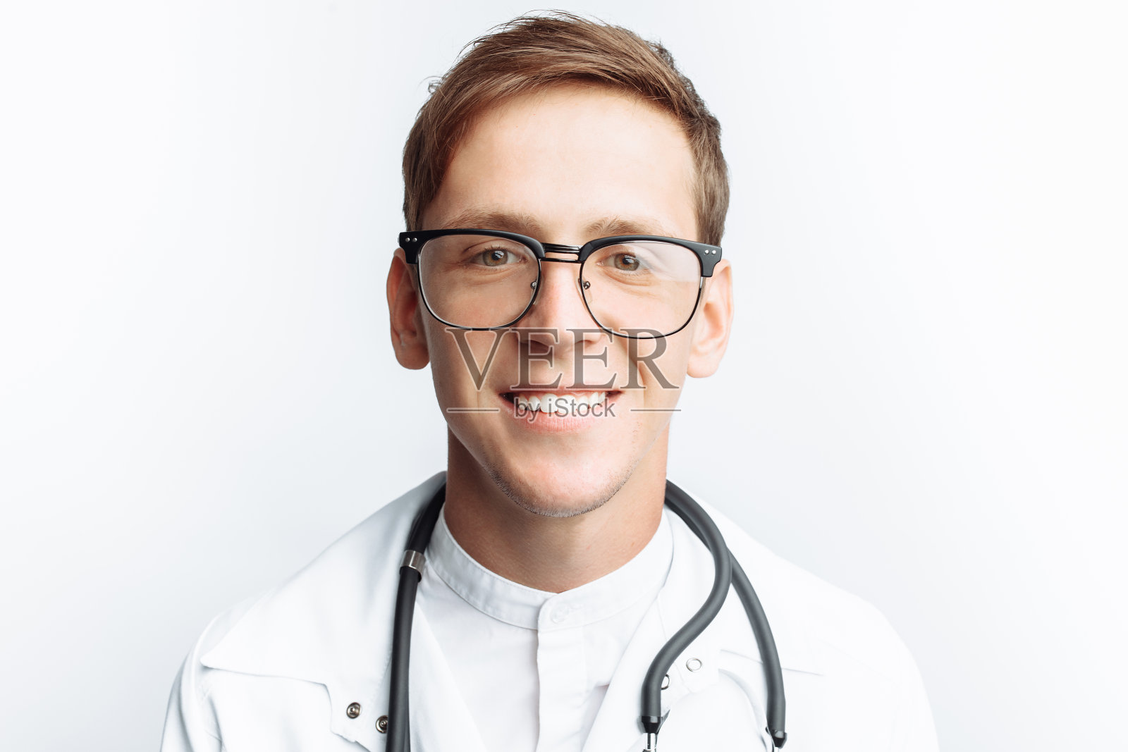 一个年轻医生的肖像特写在一个白色的背景，手的特写持有一个听诊器与听诊器在颈部照片摄影图片