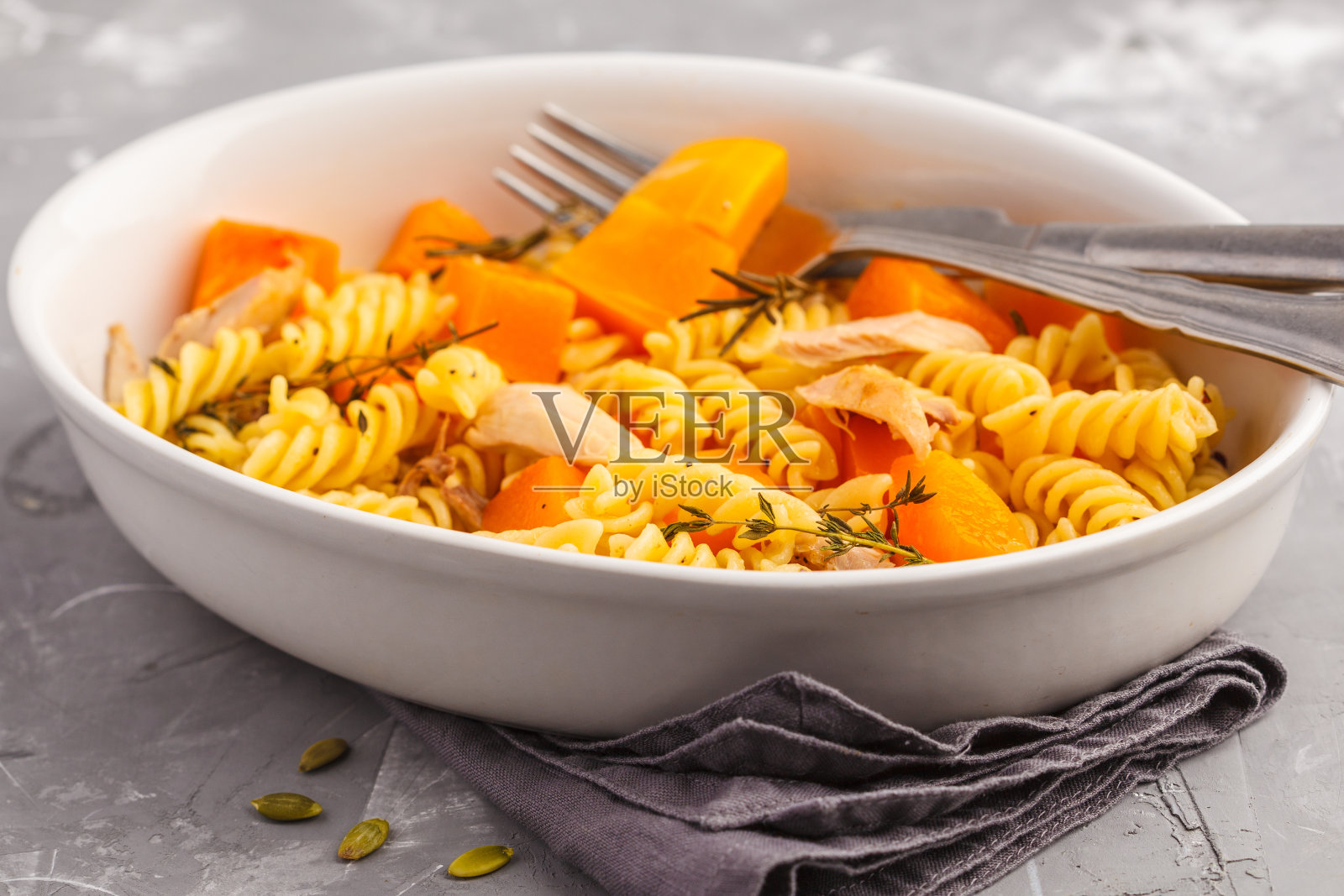 灰色背景的白色盘子里有烤南瓜和鸡肉的意大利面。健康食品的概念。照片摄影图片