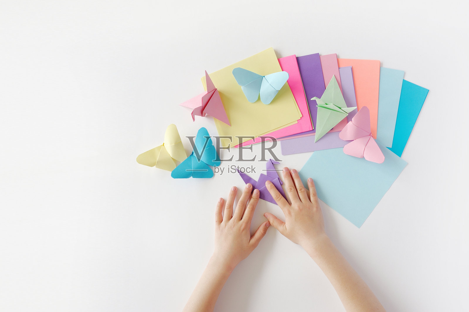 孩子们的手用彩色纸在白色背景上折纸。折纸课照片摄影图片