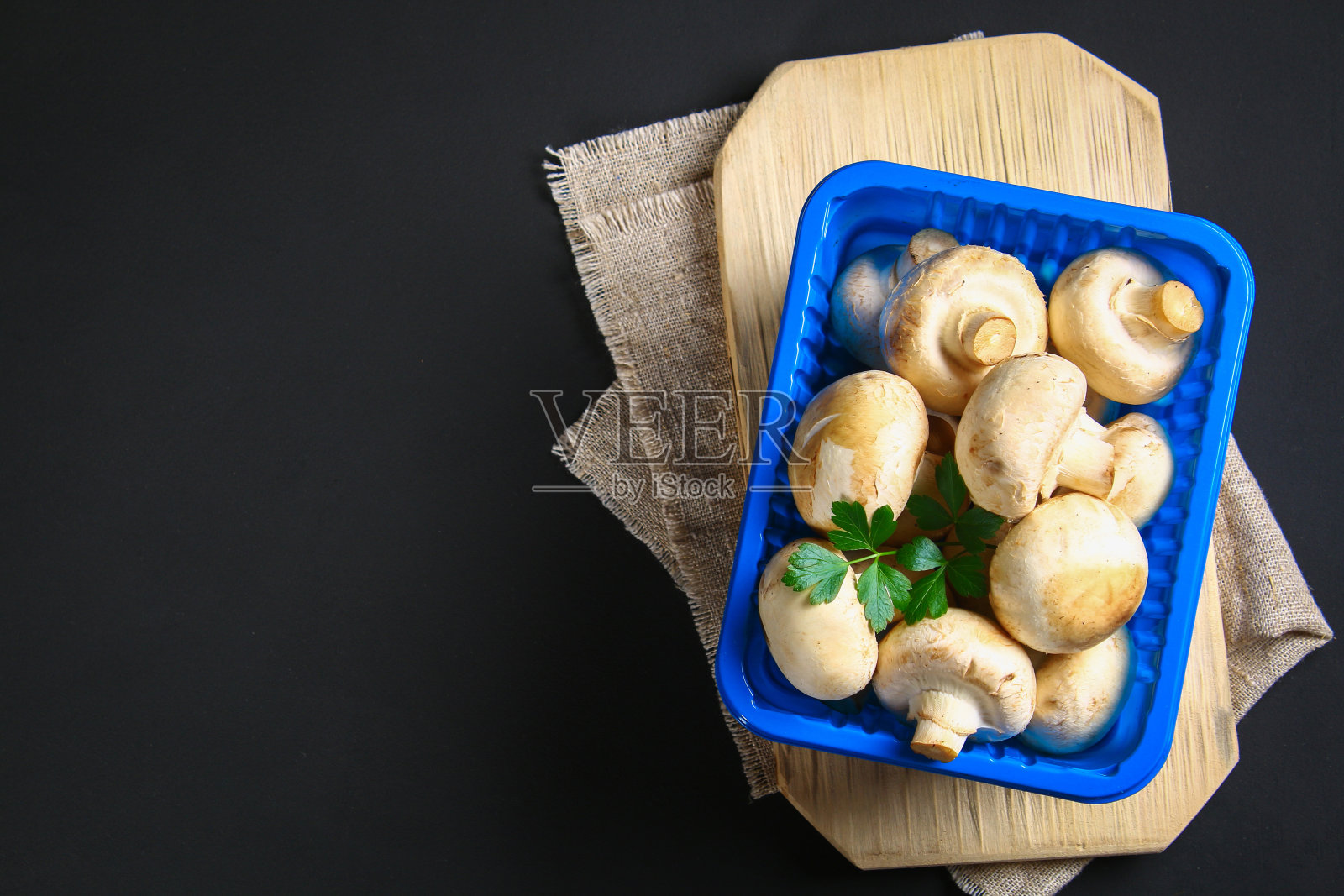 灰色深色的桌子上，木板上放着新鲜的白色香槟和欧芹。蘑菇。复制的空间。前视图。照片摄影图片