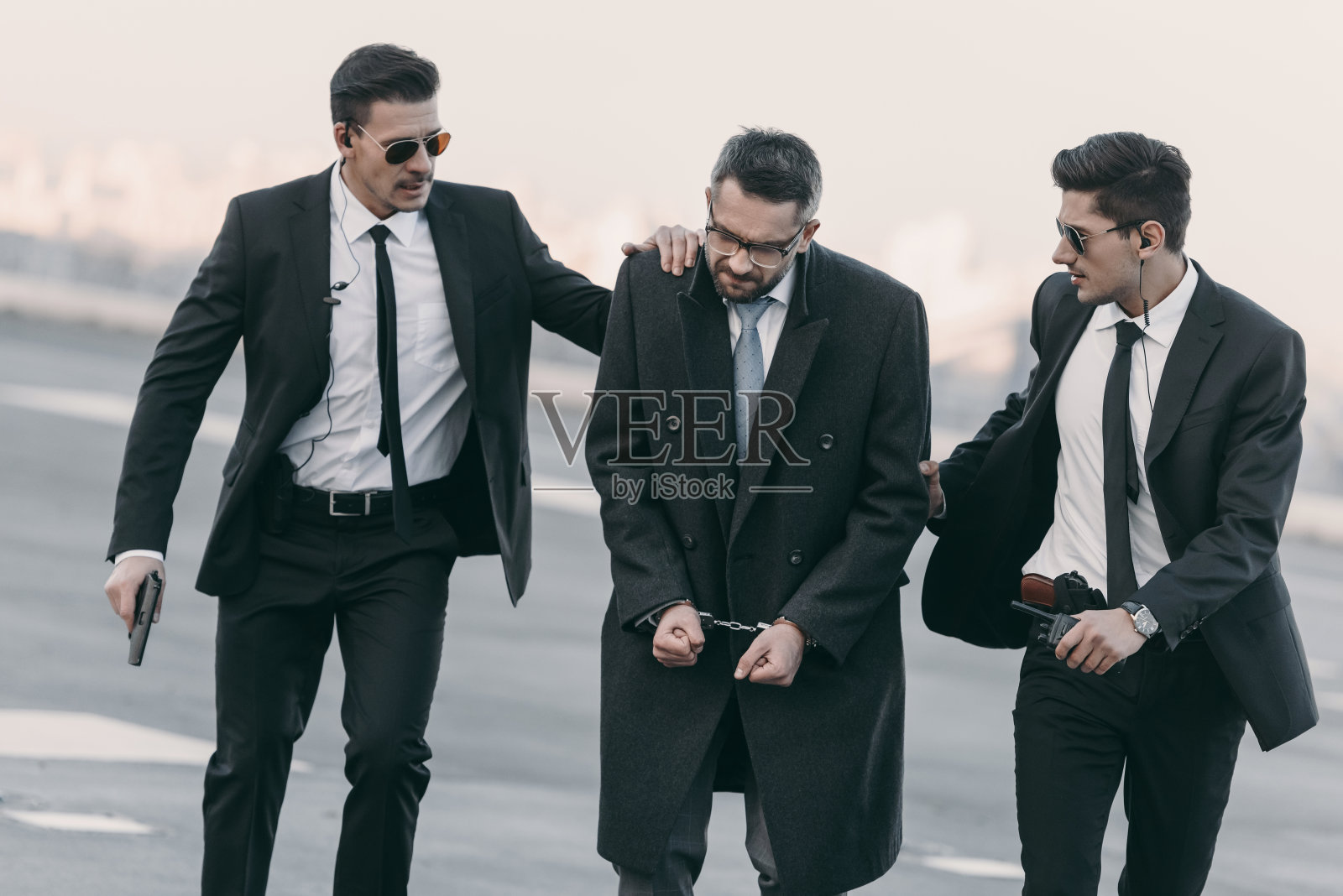 手持武器的保安和戴着手铐的被捕男子站在直升机停机坪上照片摄影图片