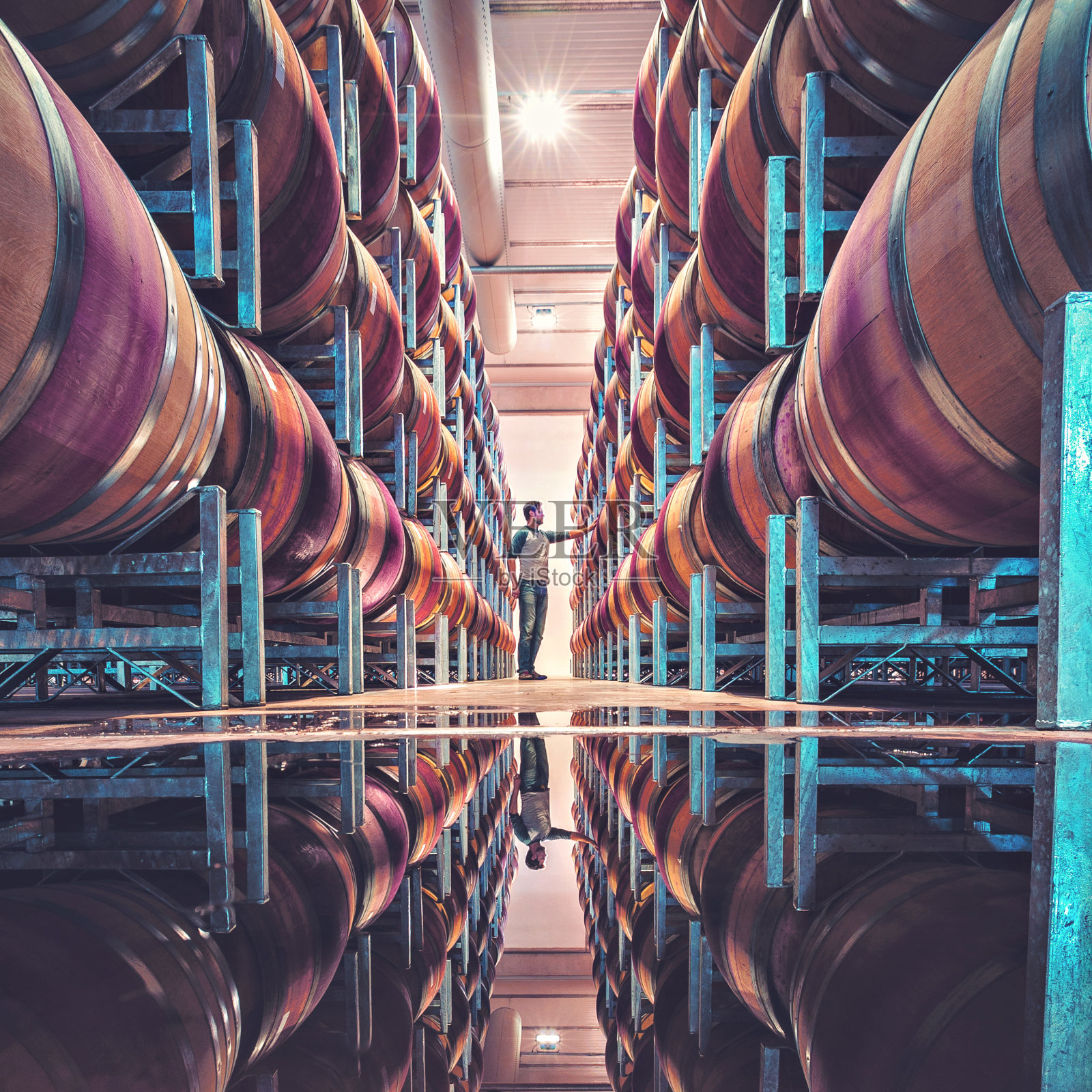 一名男子站在一排堆叠的酒桶之间，酒桶的倒影在地板上照片摄影图片