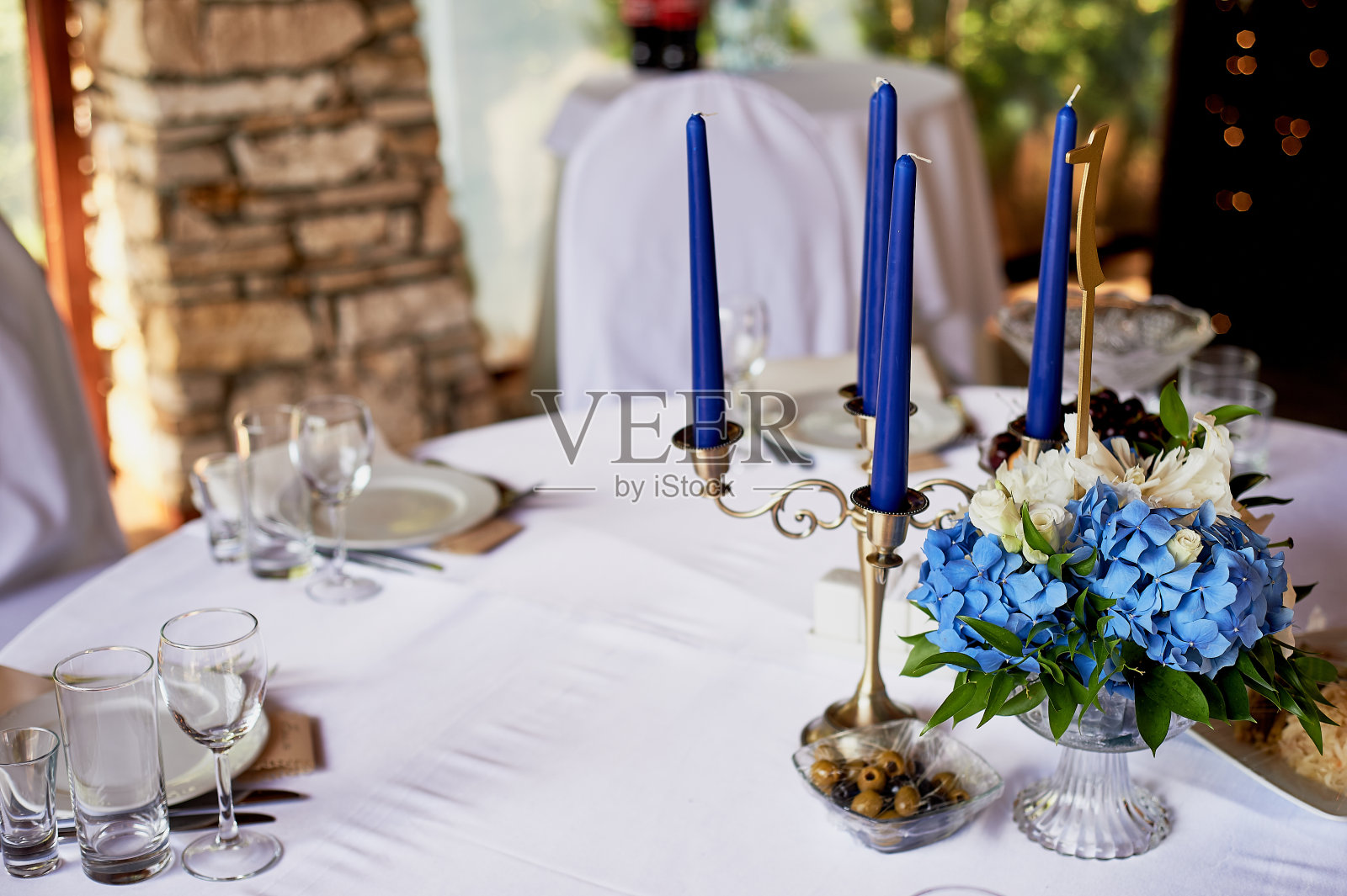 经典设计的桌子。一个装有绣球花和百合花的高花瓶，一个金色的烛台，上面有蓝色的蜡烛。装饰和花艺照片摄影图片
