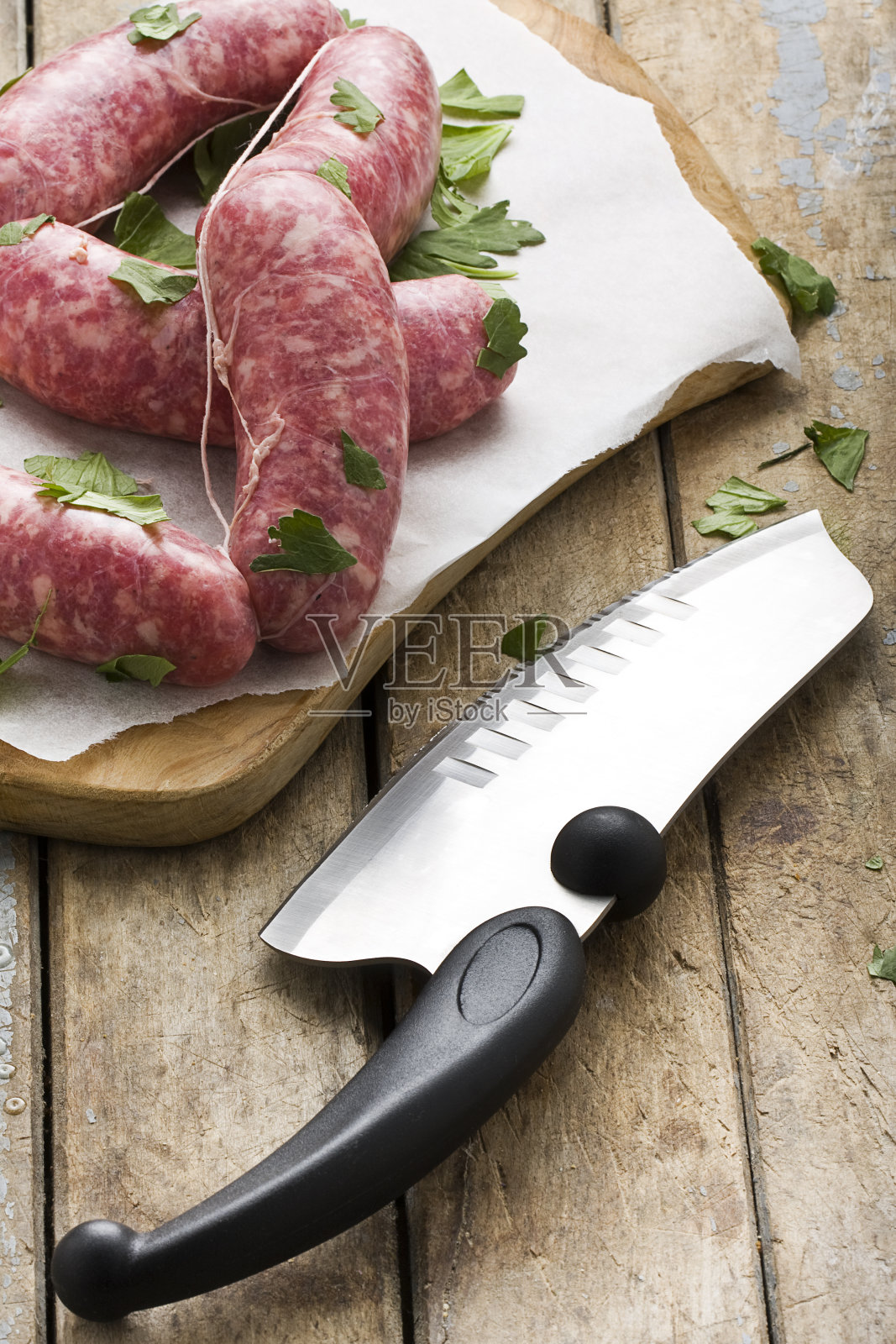 烤盘上放着生香肠和香草，旁边是简陋的木桌上的屠刀照片摄影图片