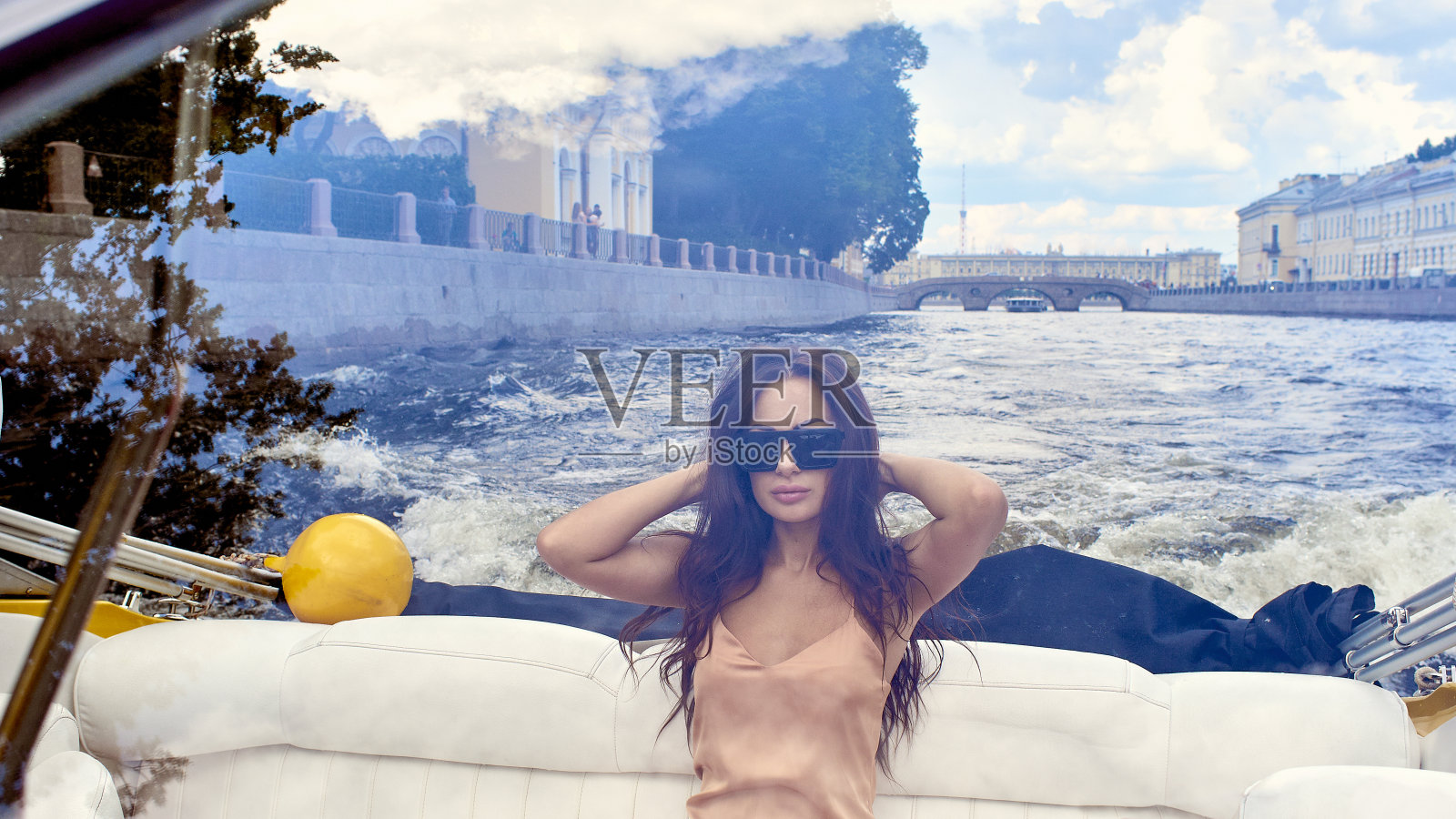 一个戴着墨镜穿着裙子坐着快艇的黑发姑娘的肖像。照片摄影图片