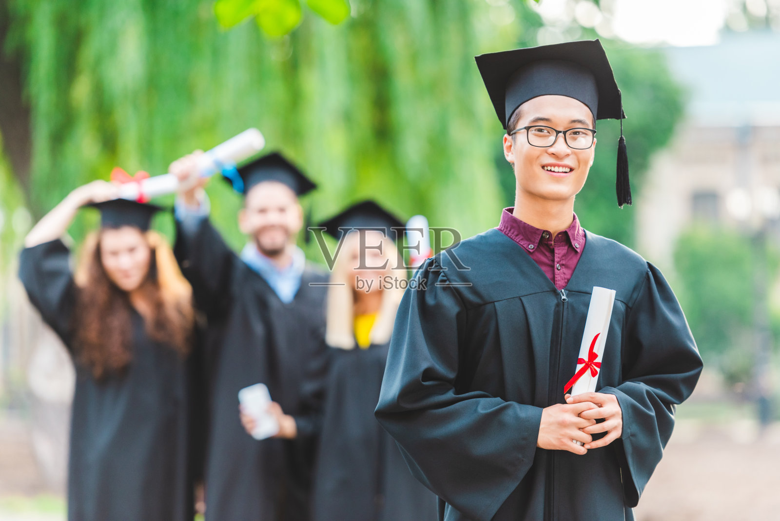 在夏季公园里，微笑的亚洲毕业生和落后的同学们选择性的聚焦照片摄影图片