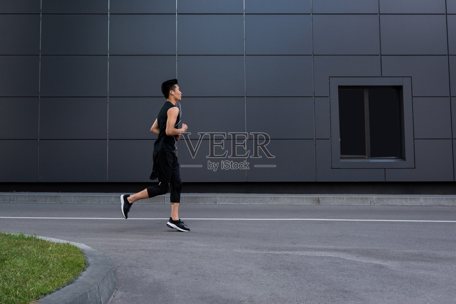 侧面的年轻亚洲运动员戴着耳机在城市街道上跑步照片摄影图片