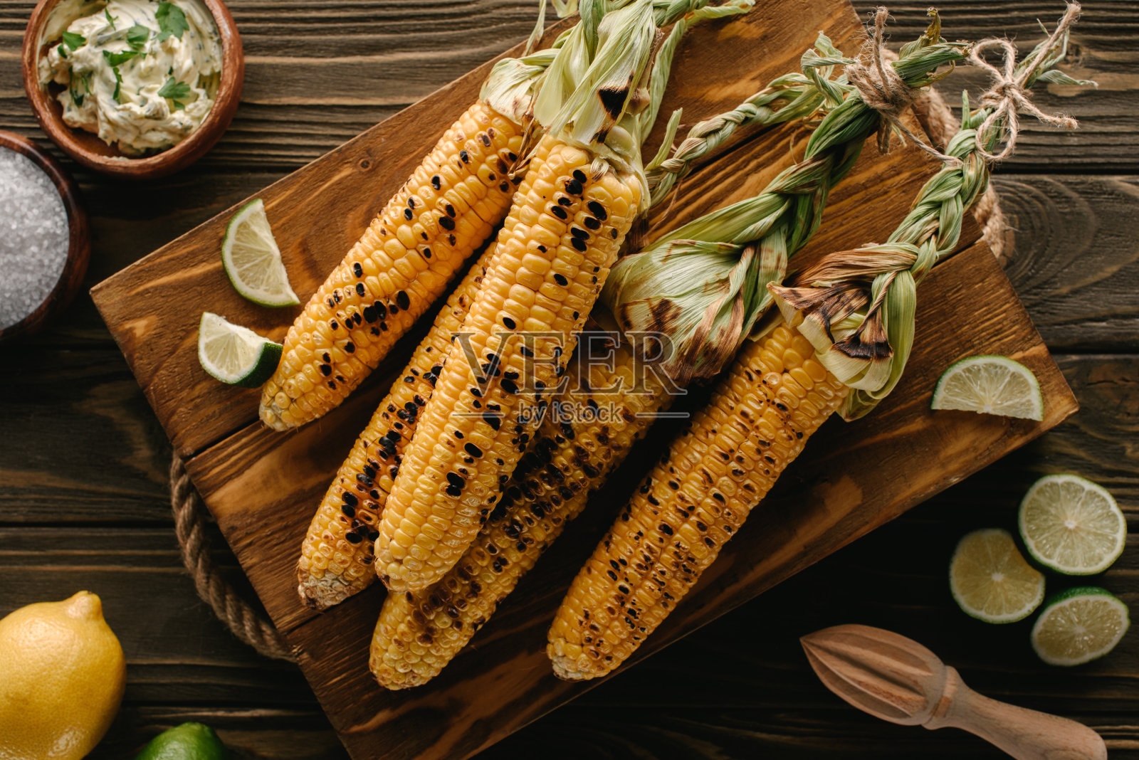 俯视图切板与烤玉米，酸橙片，盐，柠檬，黄油与欧芹和挤压在木桌上照片摄影图片
