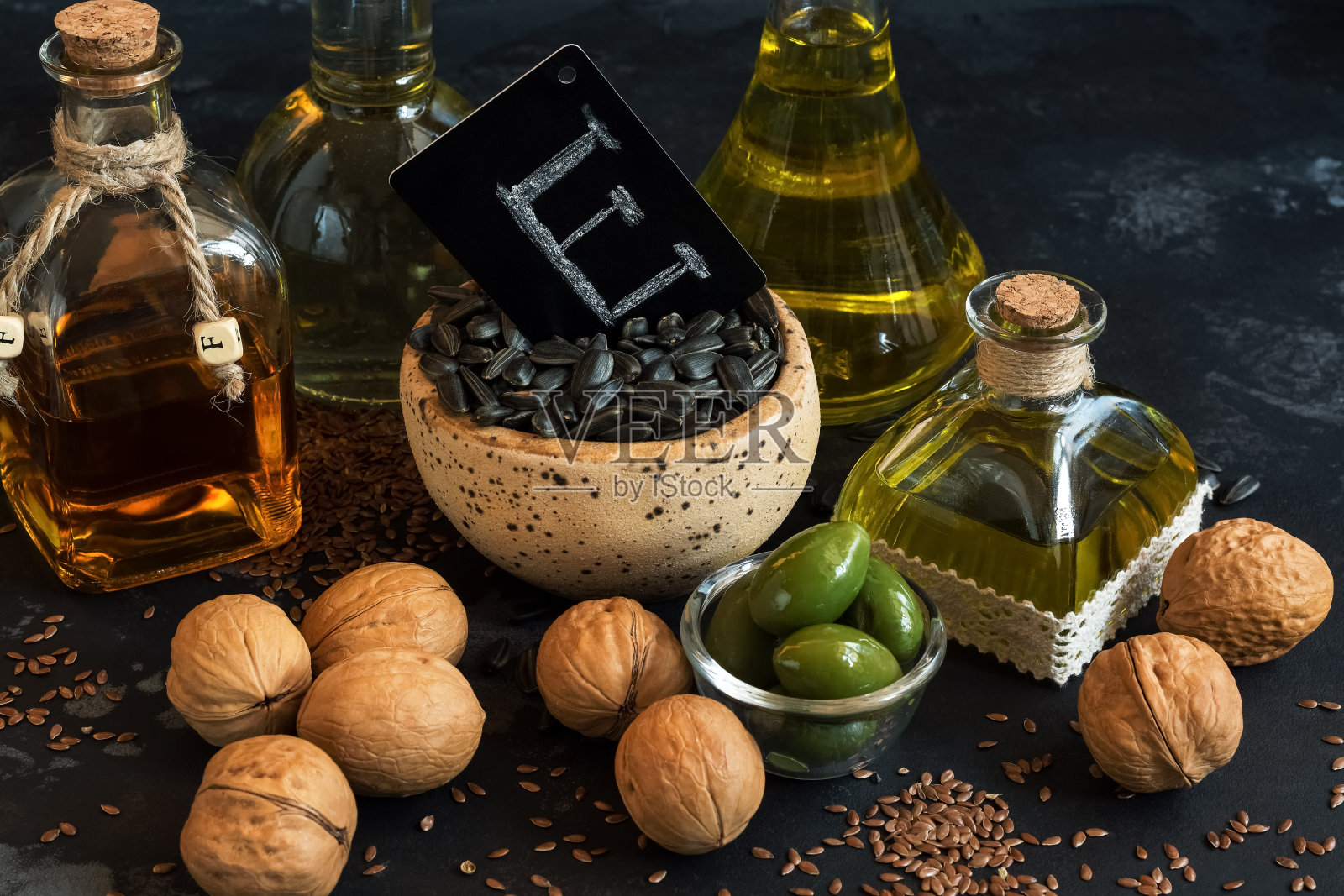 特写产品与维生素e橄榄油，亚麻籽，核桃和向日葵在黑色混凝土背景。有选择性的重点。照片摄影图片