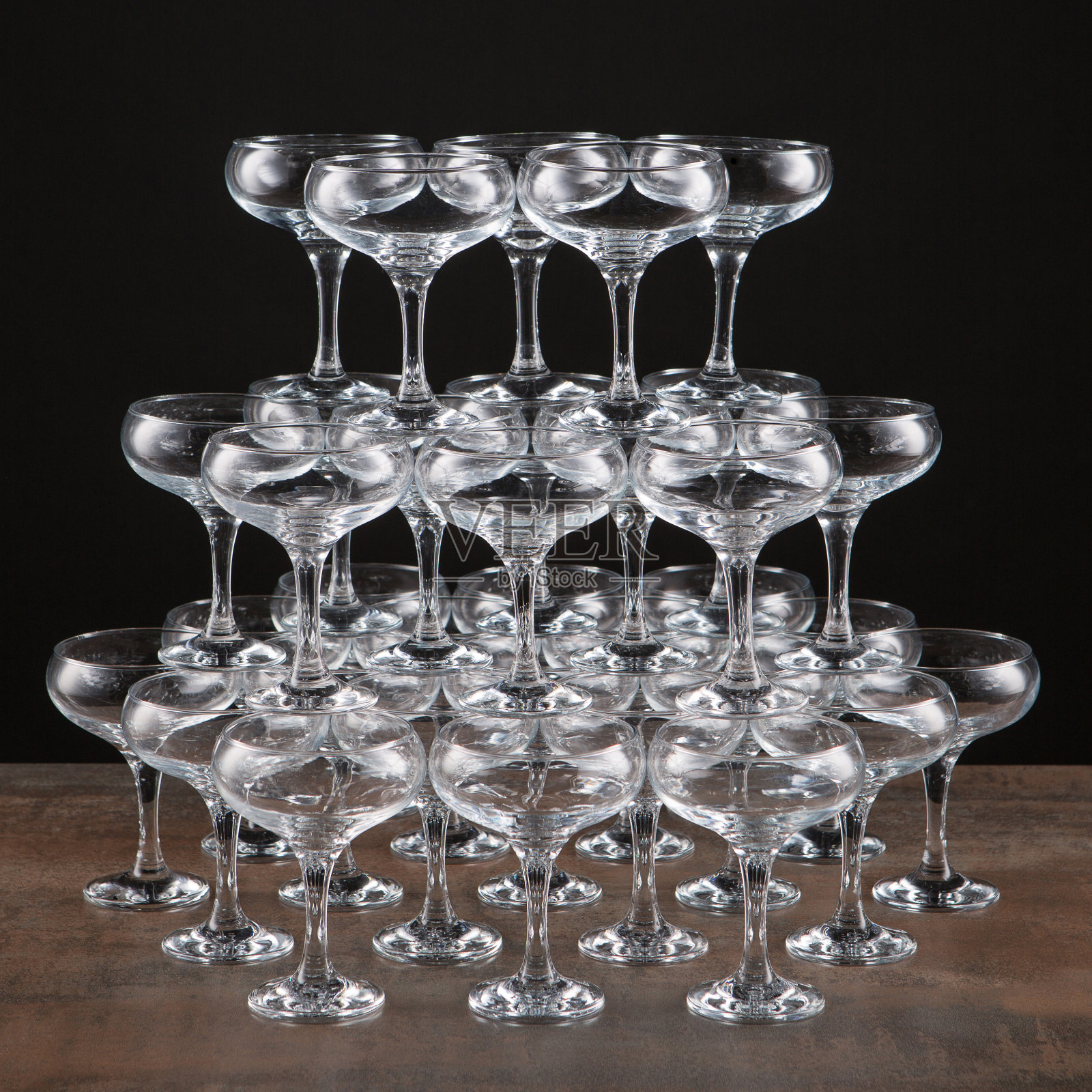 一张棕色的桌子上放着很多空酒杯，桌子是由高高的金字塔建造的，桌子的背景是黑色的，孤立无间照片摄影图片