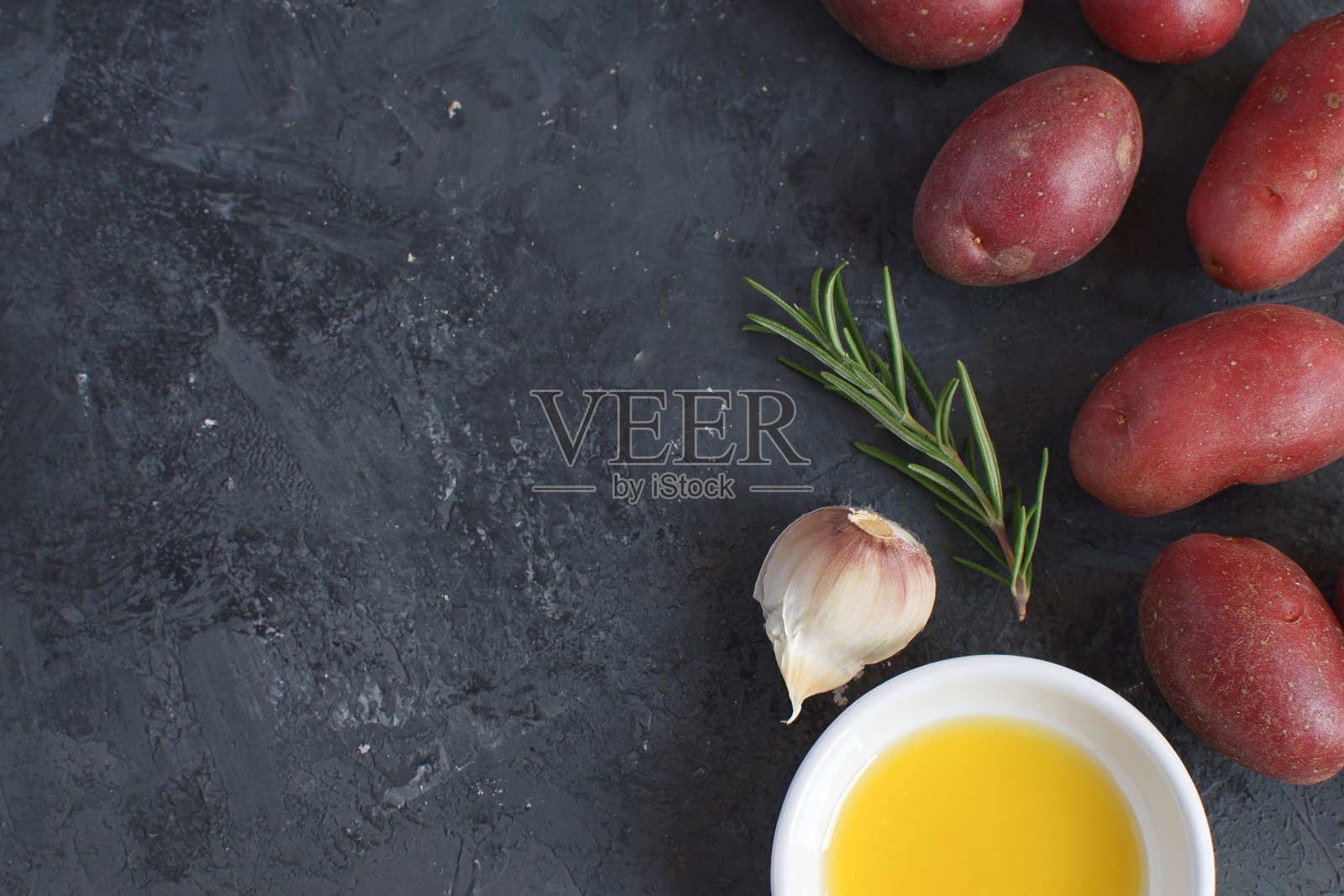 橄榄油、瓷盘、迷迭香枝、混合胡椒、大蒜调味料、香料、生土豆，烹饪理念，黑色水泥背景，顶部视图，复制空间，扁平风格照片摄影图片