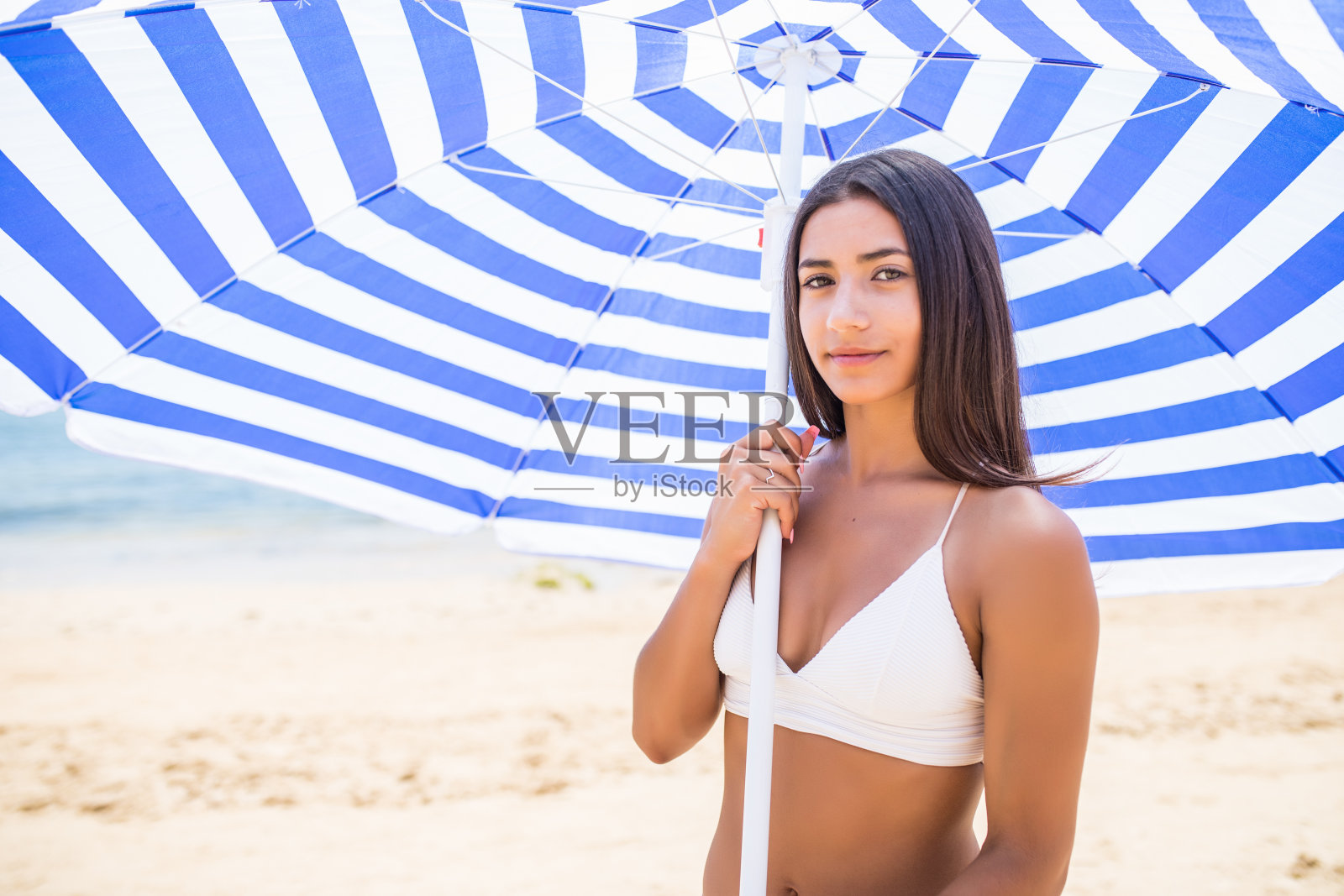 防晒和夏季身体护理概念。年轻的拉丁女人在沙滩伞下穿着比基尼照片摄影图片