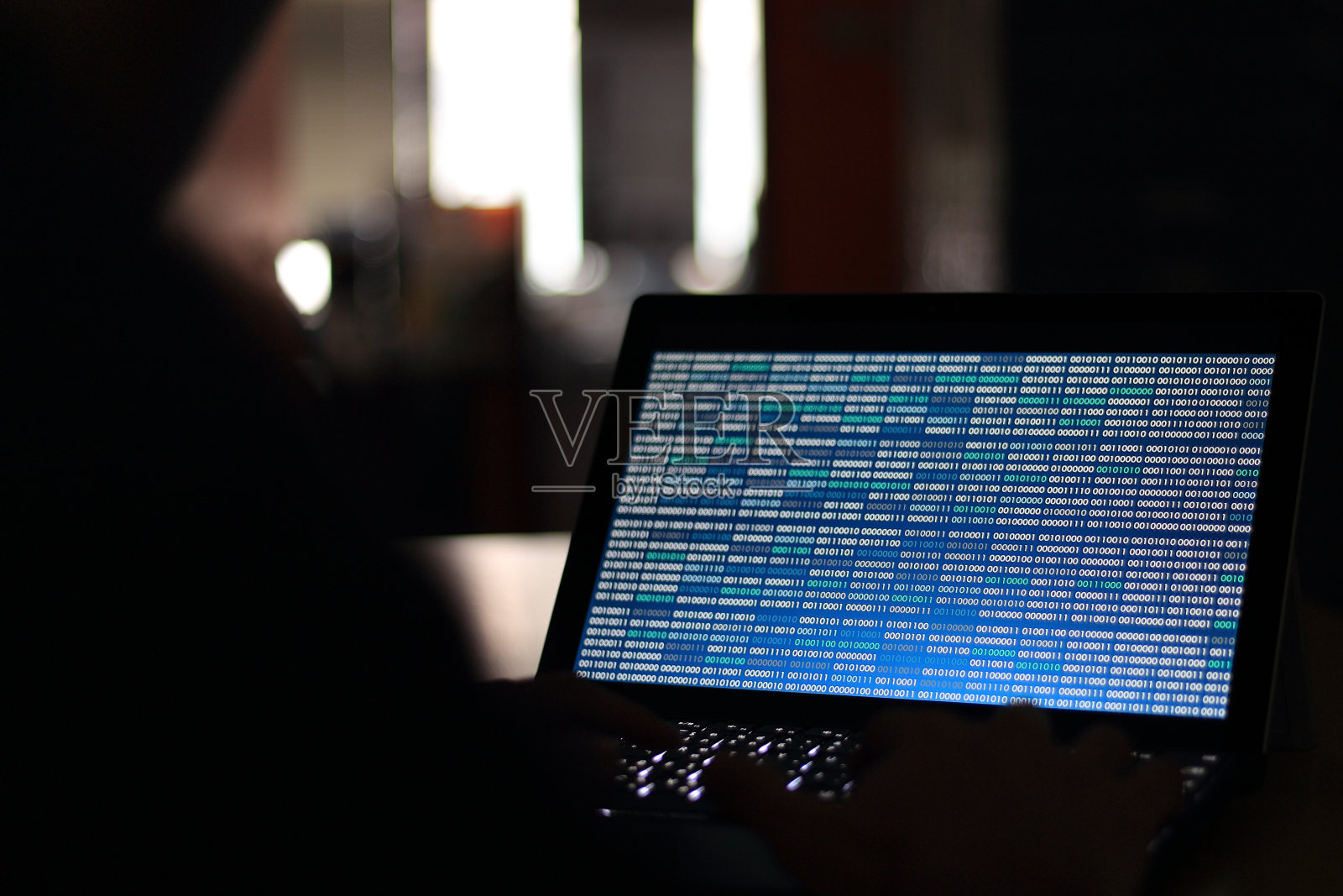 电脑黑客在一间黑屋子里用电脑打字。致力于蓝色二进制代码技术。二进制数据，计算机编程和网络安全概念。照片摄影图片