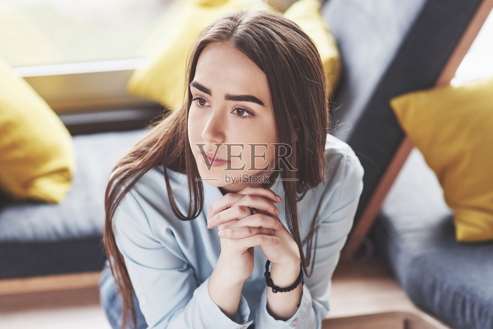 美丽的年轻女孩在娱乐区度过她的时间。她坐在靠近窗户的六边形沙发椅上玩得很开心照片摄影图片