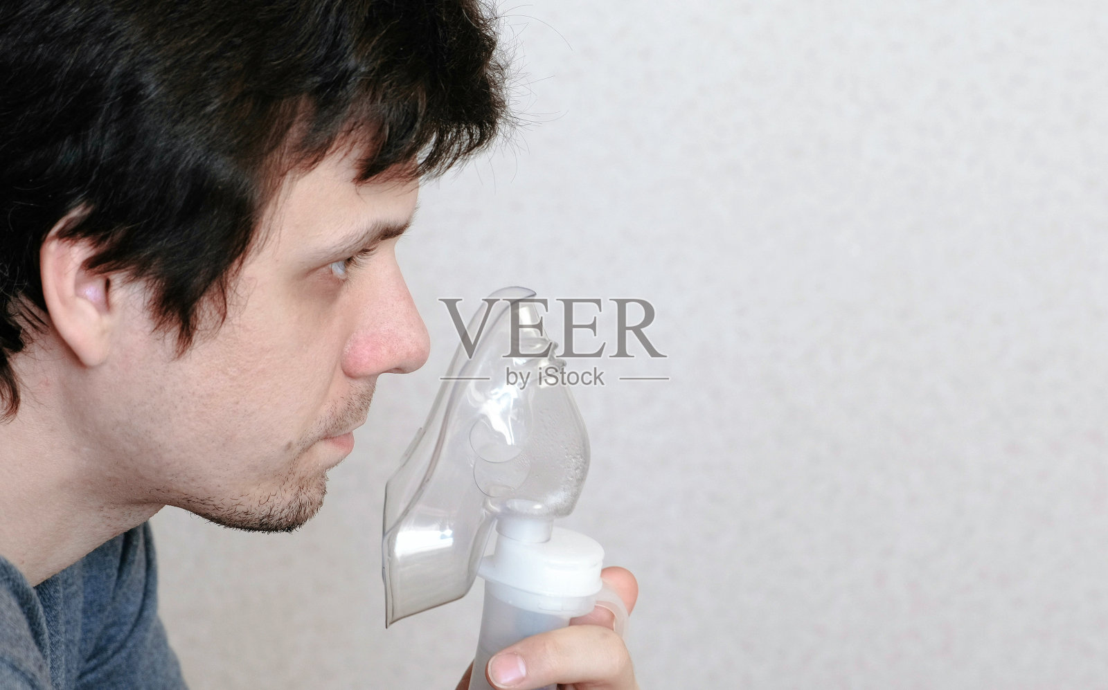 使用喷雾器和吸入器进行治疗。特写年轻人的脸通过吸入器口罩吸入。侧视图照片摄影图片