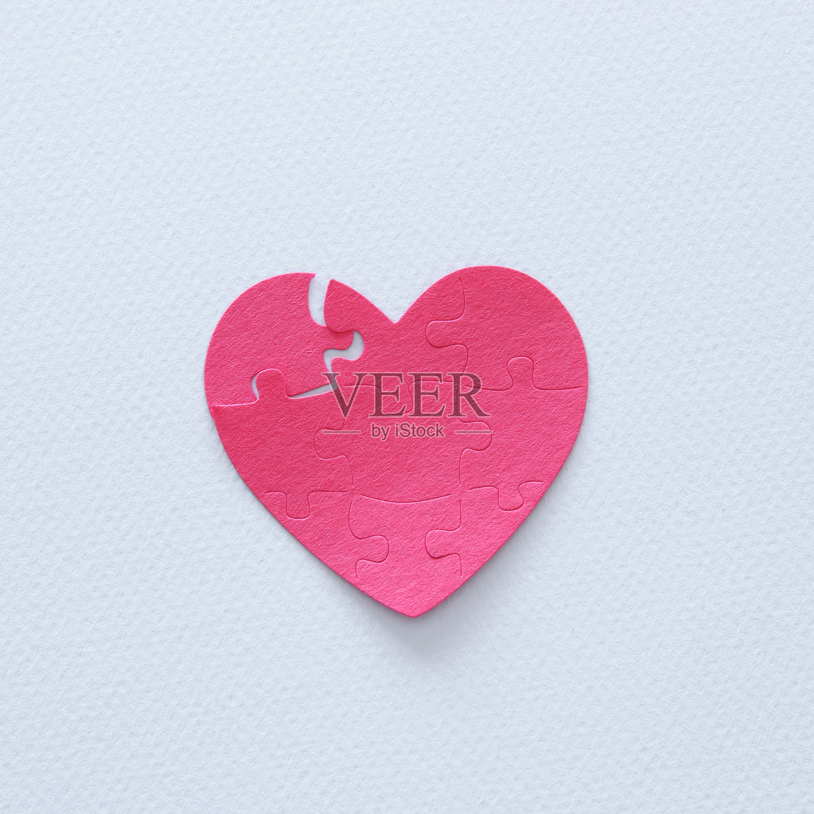 白色背景上缺少一块的粉色纸质心形拼图俯视图：关于医疗保健、捐赠、世界心脏日和世界卫生日照片摄影图片
