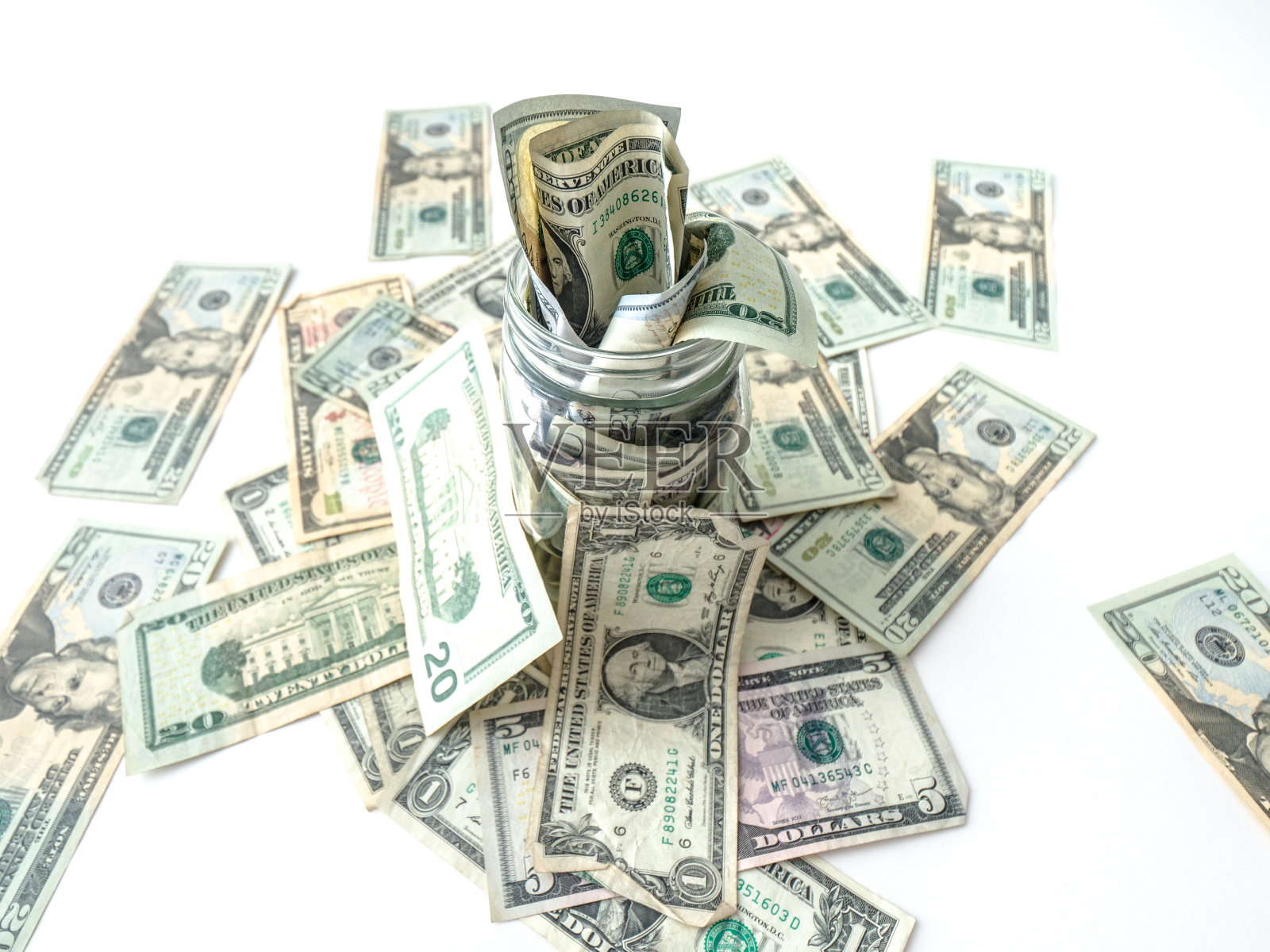 这是一张美国现金或纸币从一个玻璃罐中溢出并落在白色背景上的特写照片。照片摄影图片