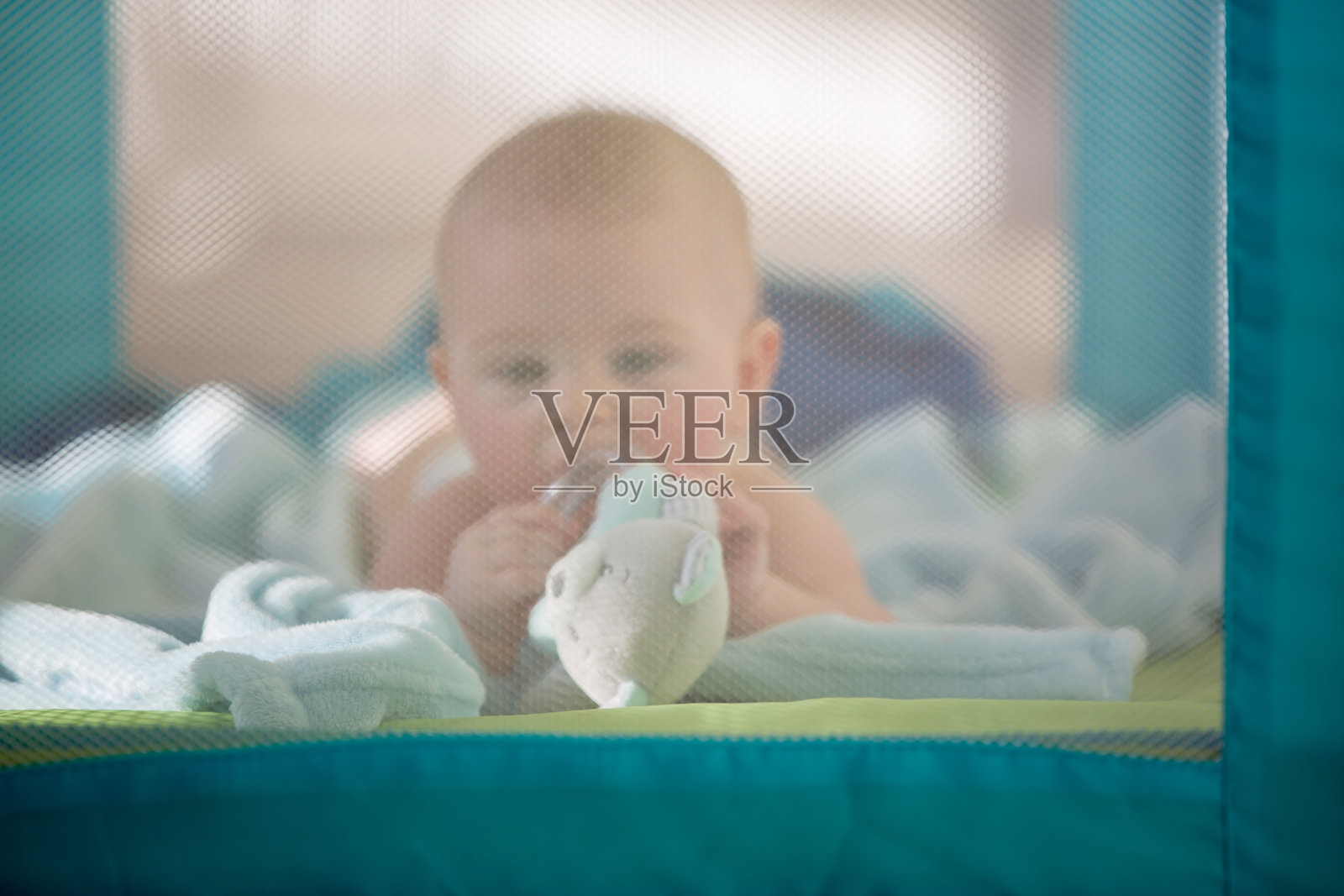 一个可爱的小男孩，在一个阳光明媚的日子里在一个移动的婴儿床里玩玩具照片摄影图片