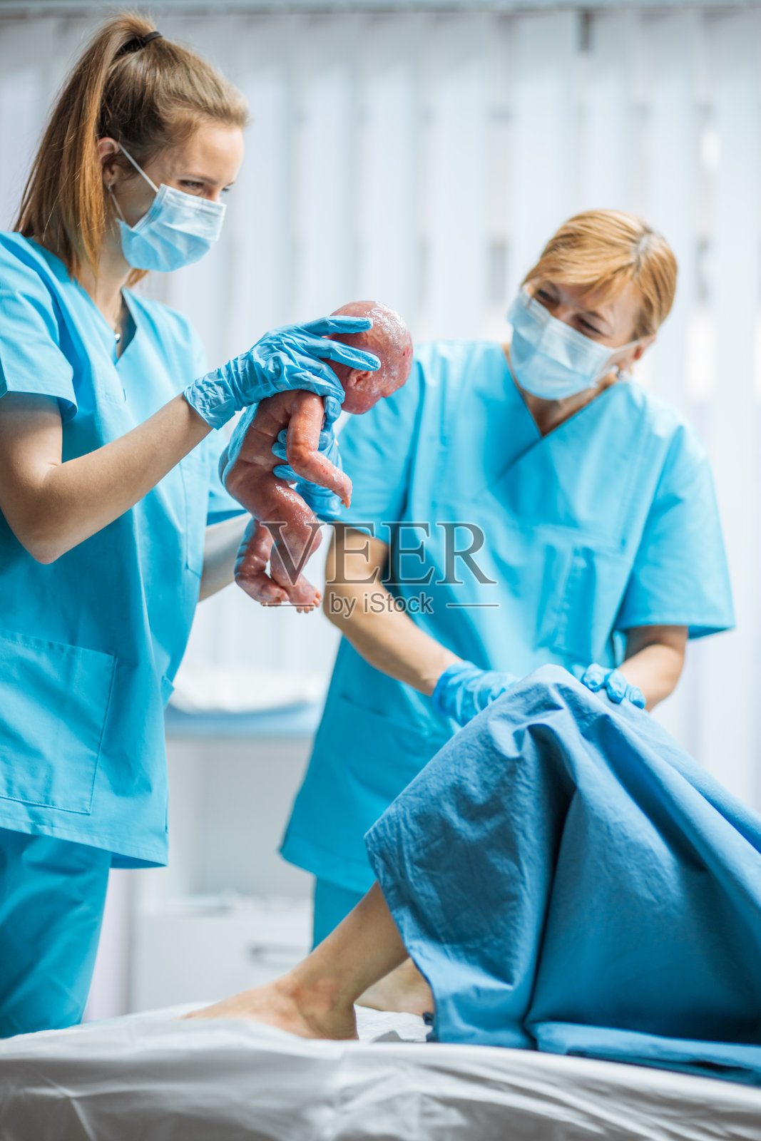 在医院里，待产妇女推着孩子，婴儿出来了，产科医生抱着婴儿。侧面镜头。照片摄影图片