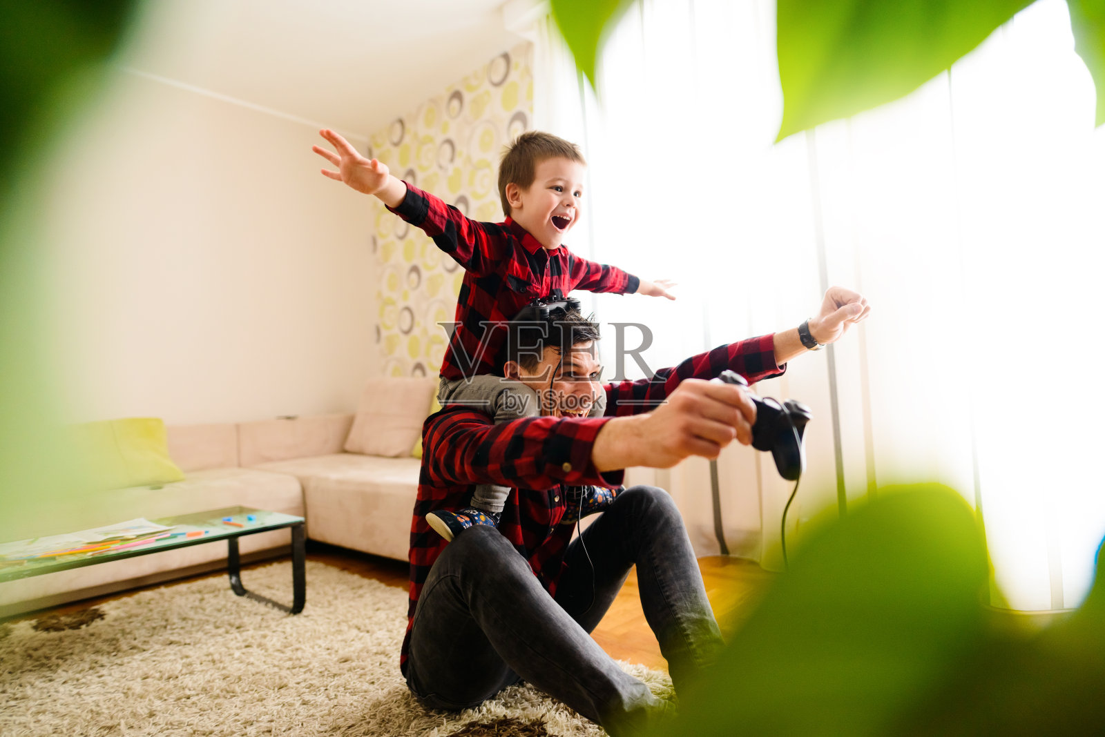 快乐的父亲和儿子庆祝赢得电子游戏的第一名。儿子坐在父亲的背上，举起手臂。照片摄影图片