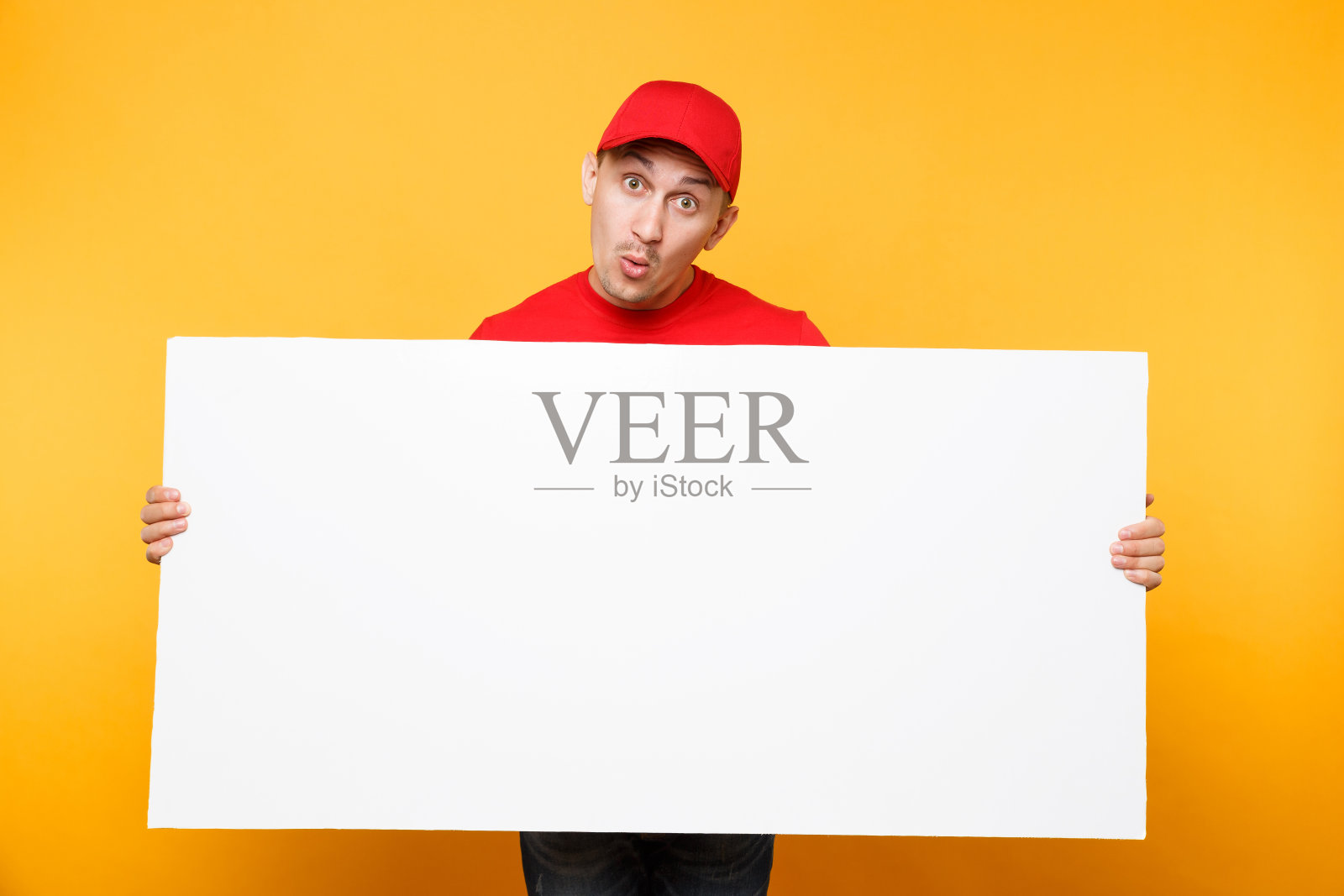身穿红色制服的送货员被隔离在黄橙色背景下。男员工快递员戴着便帽，t恤上拿着大大的空白空白广告牌与文案空间，放置文字图像。服务的概念。照片摄影图片