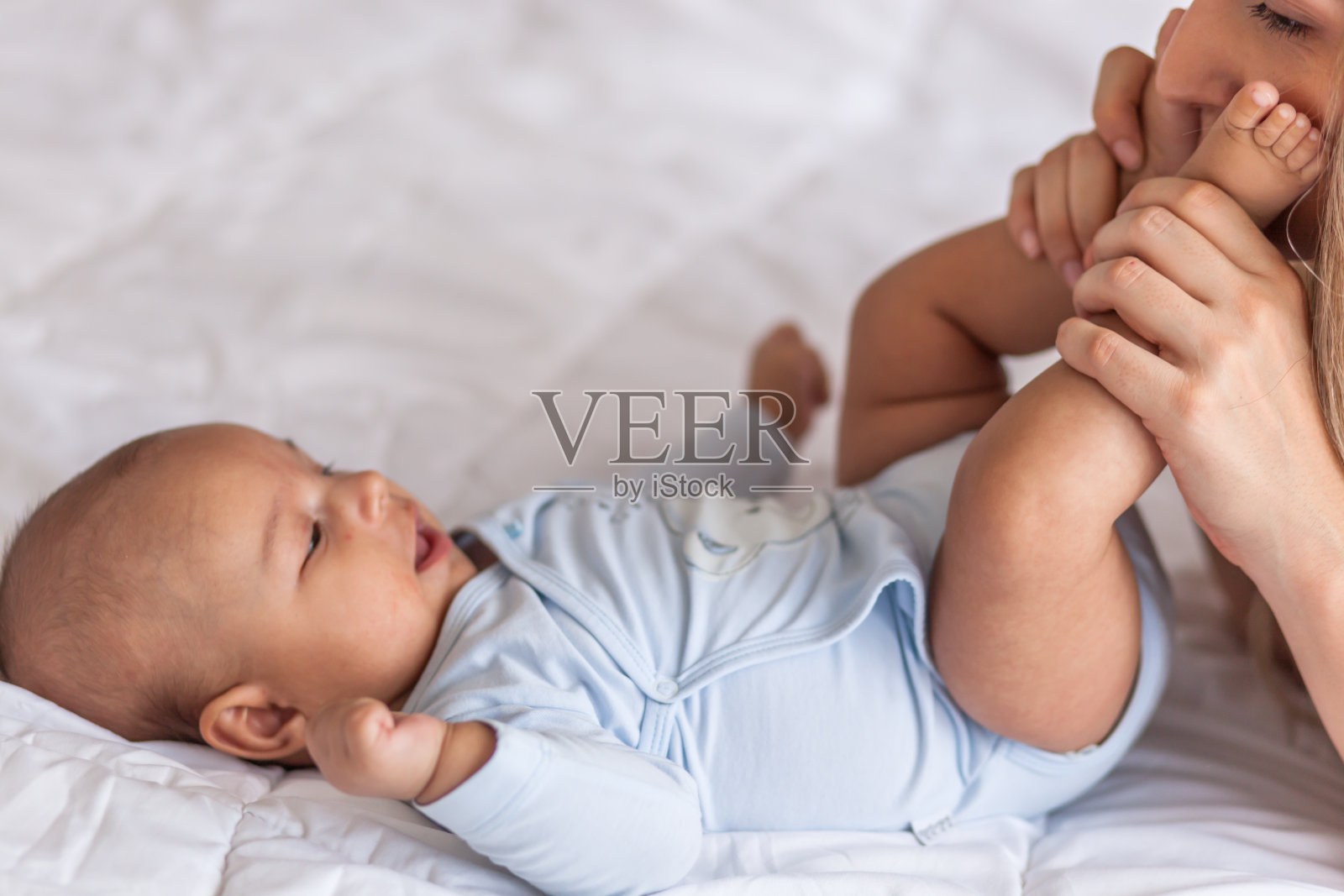 母亲和孩子在一张白色的床上。妈妈和小男孩在阳光明媚的白色卧室里玩耍。父母和孩子在家里放松。照片摄影图片