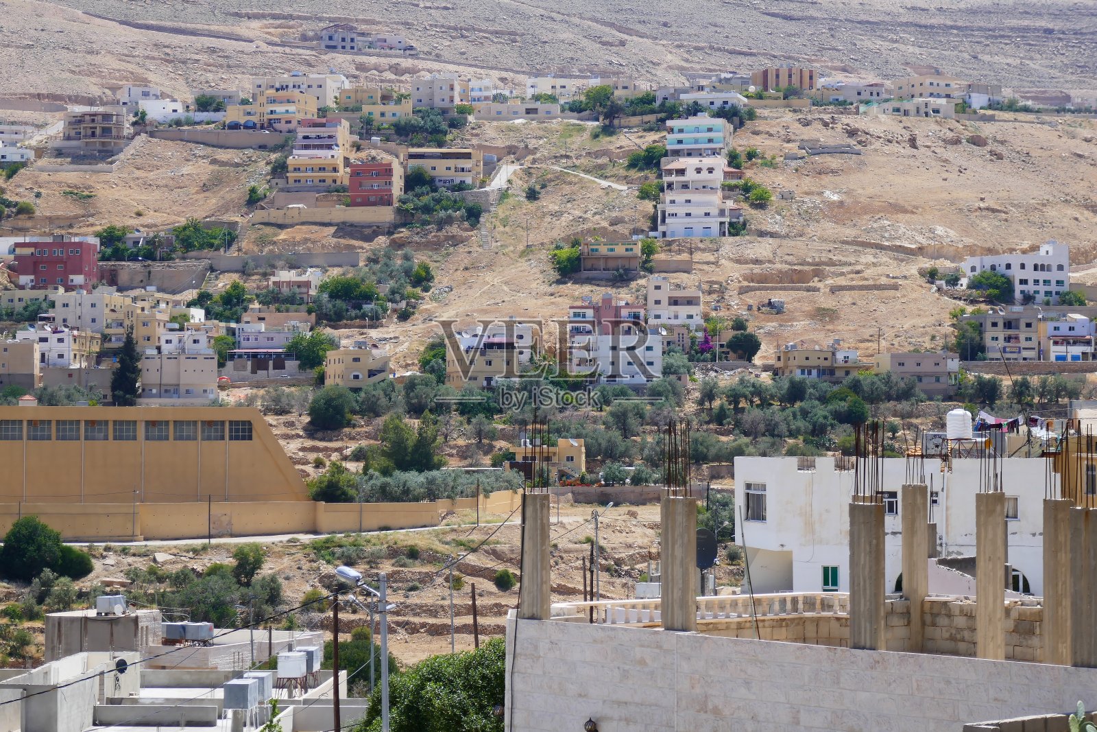 许多色彩斑斓的房子坐落在约旦贫瘠的岩石山坡上，前景是建筑工程照片摄影图片
