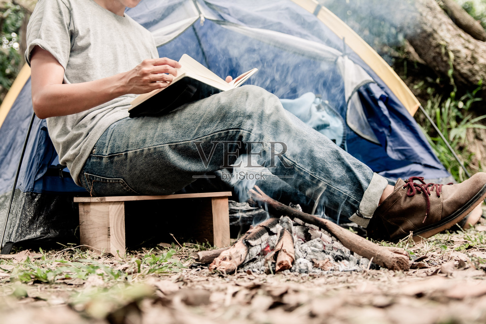 一个亚洲年轻人坐在帐篷外看书。独自在森林里露营。照片摄影图片