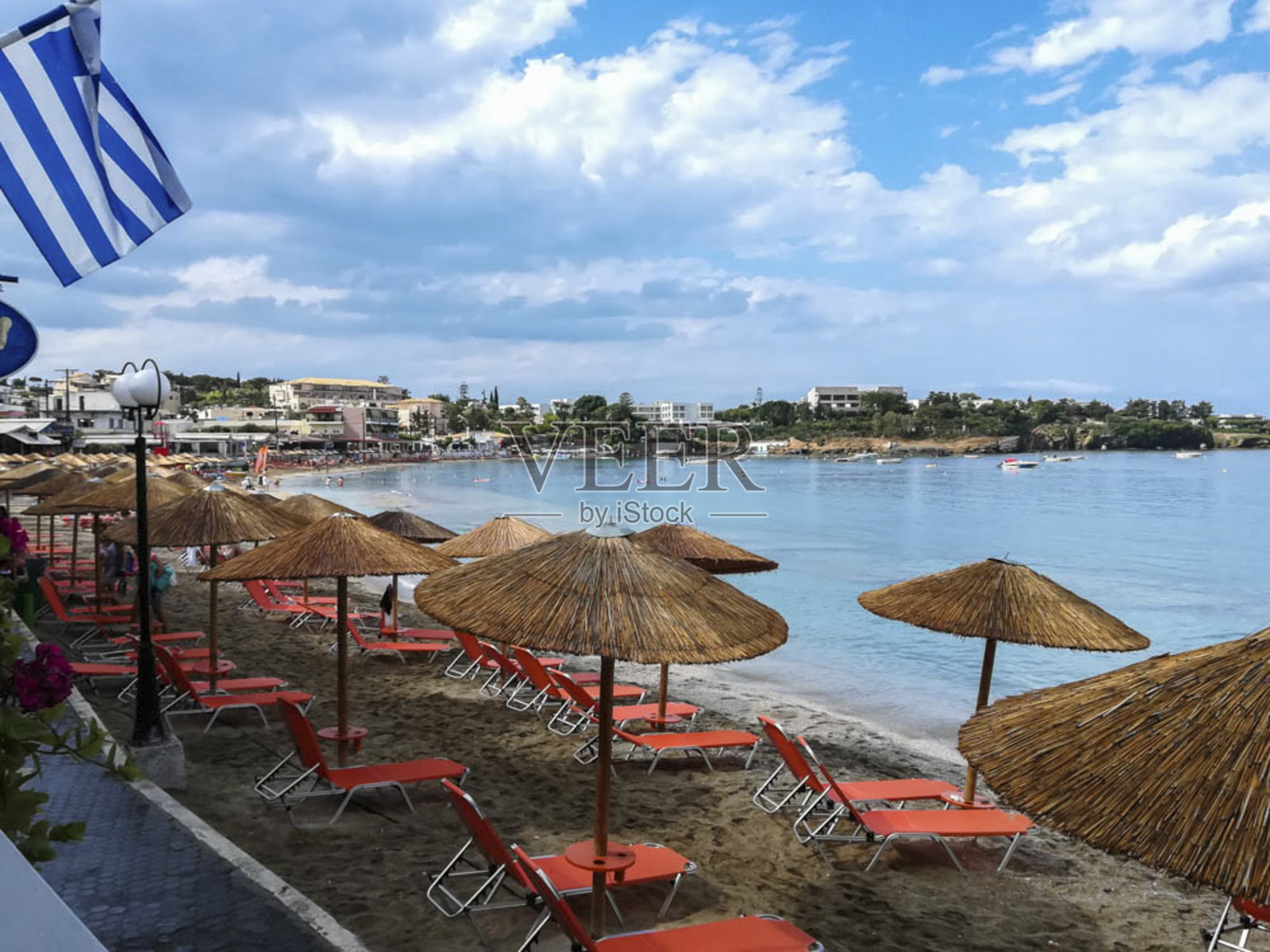 这是希腊克里特岛海滩上的一张照片，上面有木制的雨伞，清澈的蓝天和希腊国旗照片摄影图片