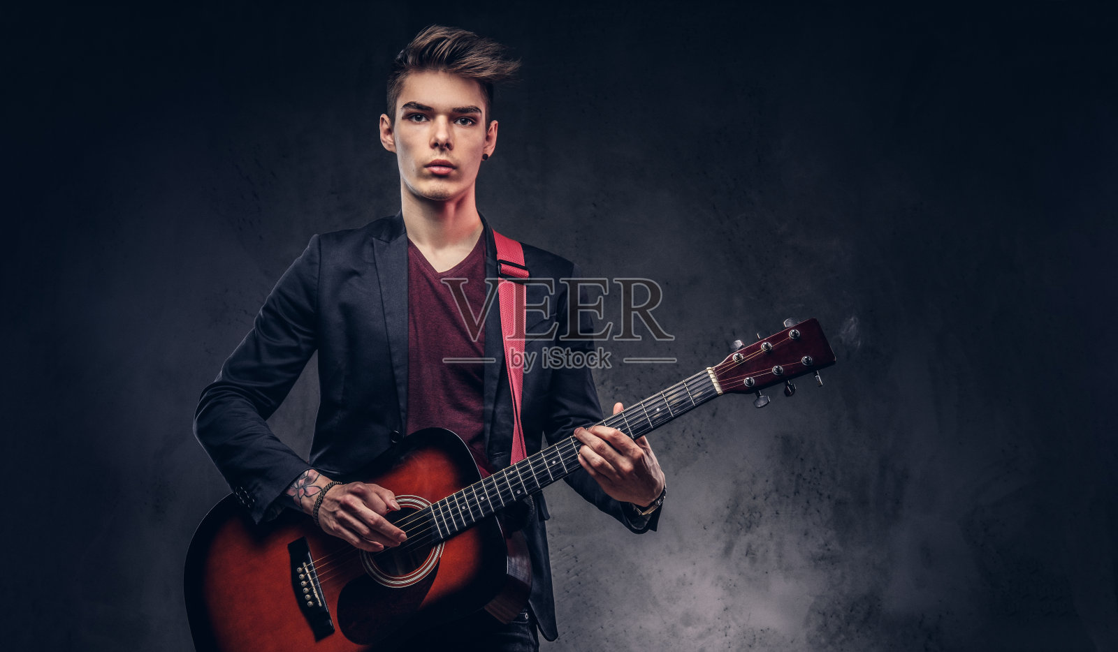 有型的年轻音乐家，有型的头发，优雅的衣服，弹奏着原声吉他。照片摄影图片