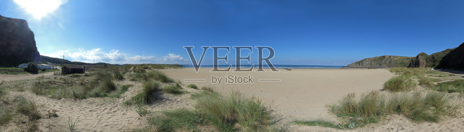 一个海滩或海湾的全景图像与沙，草，波浪，高岩石和蓝色的天空与云在一个晴朗的夏天照片摄影图片