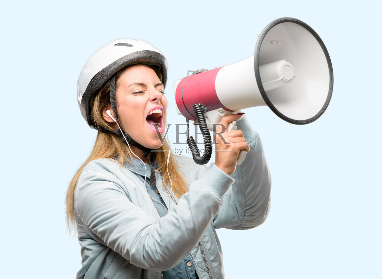 年轻女子戴着自行车头盔和耳机，手持扩音器大声喊叫，表达成功和积极的概念，营销或销售的想法照片摄影图片