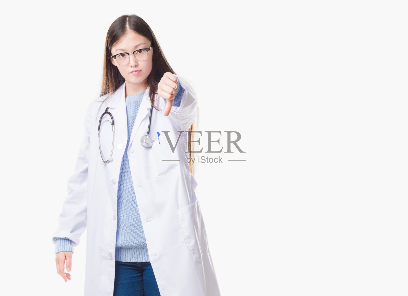 年轻的中国女医生在孤立的背景下看起来不高兴和愤怒，表示拒绝和负面的拇指向下的手势。糟糕的表达。照片摄影图片