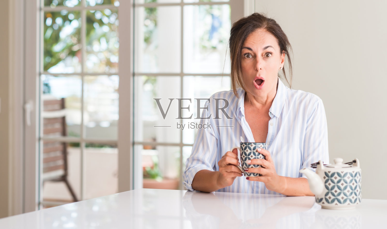 中年妇女喝着茶或咖啡惊恐地露出惊讶的表情，害怕又兴奋又害怕的表情照片摄影图片